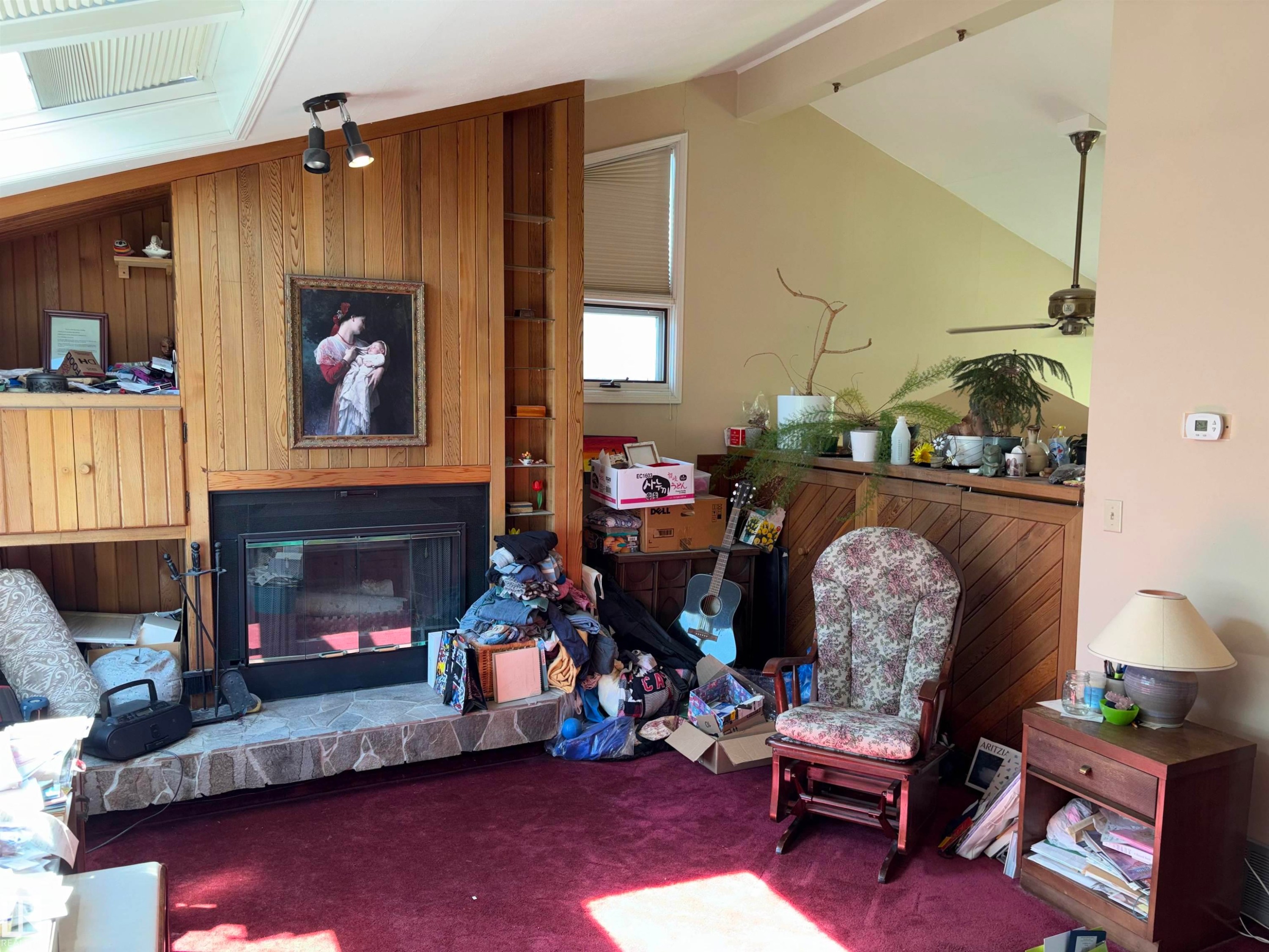 Living space featuring a stone hearth fireplace with a black iron grate, wood paneling, built-in shelving, vaulted ceilings, and a skylight - 8812 146 Street, Edmonton, AB