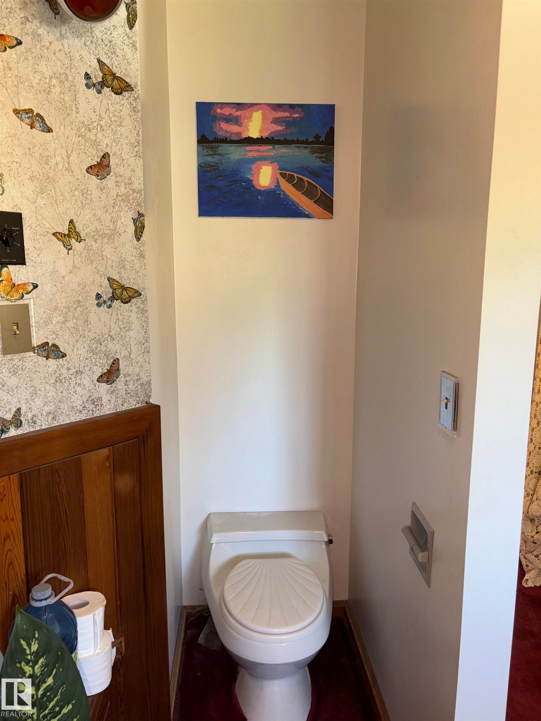 Private commode area featuring a white toilet with a fluted seat, white painted walls, and wood paneling - 8812 146 Street, Edmonton, AB