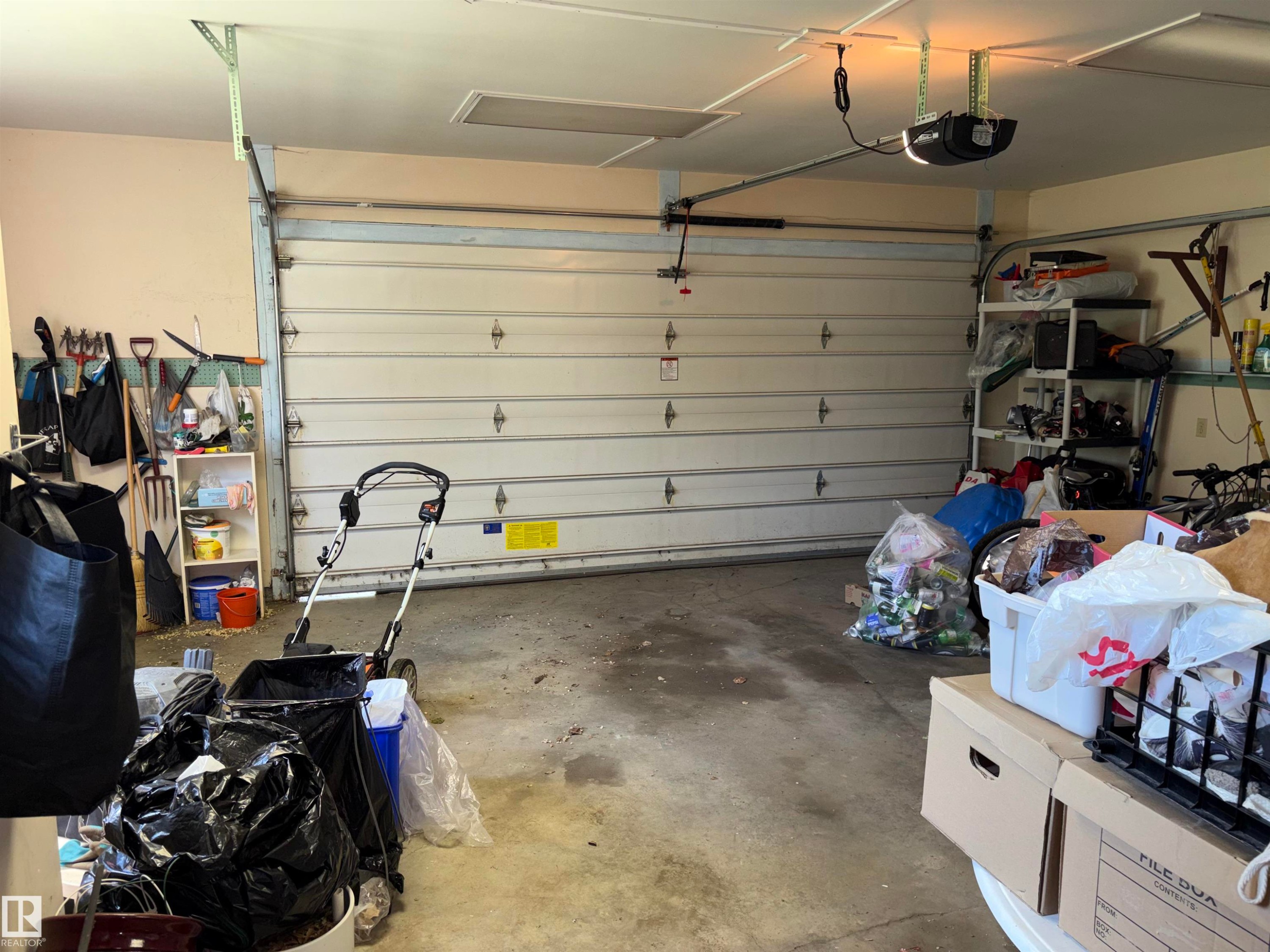 Two-car garage featuring an automatic overhead door, concrete flooring, and overhead lighting - 8812 146 Street, Edmonton, AB