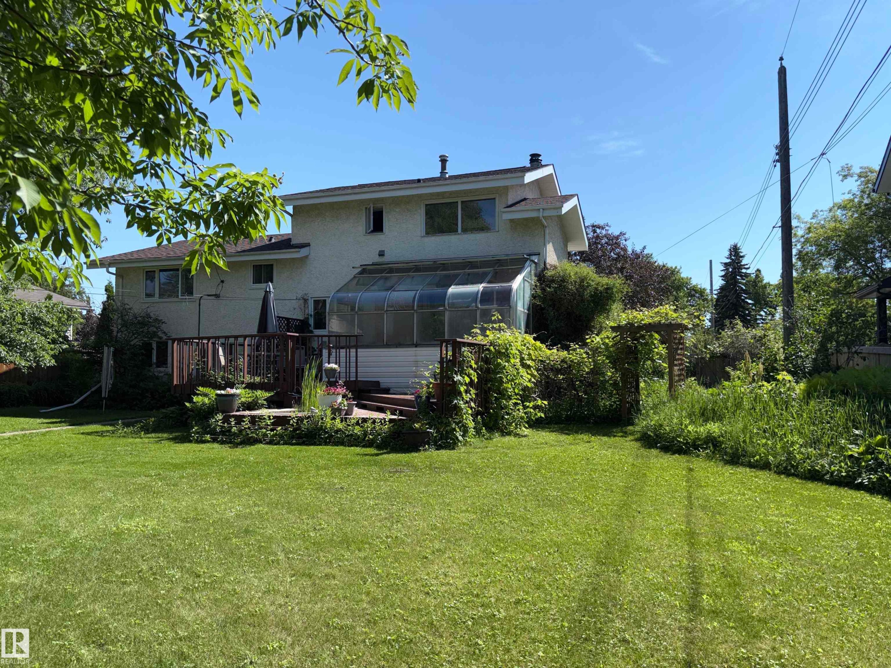 Expansive backyard featuring a manicured lawn, a multi-level wood deck, an attached sunroom, and mature perimeter landscaping - 8812 146 Street, Edmonton, AB