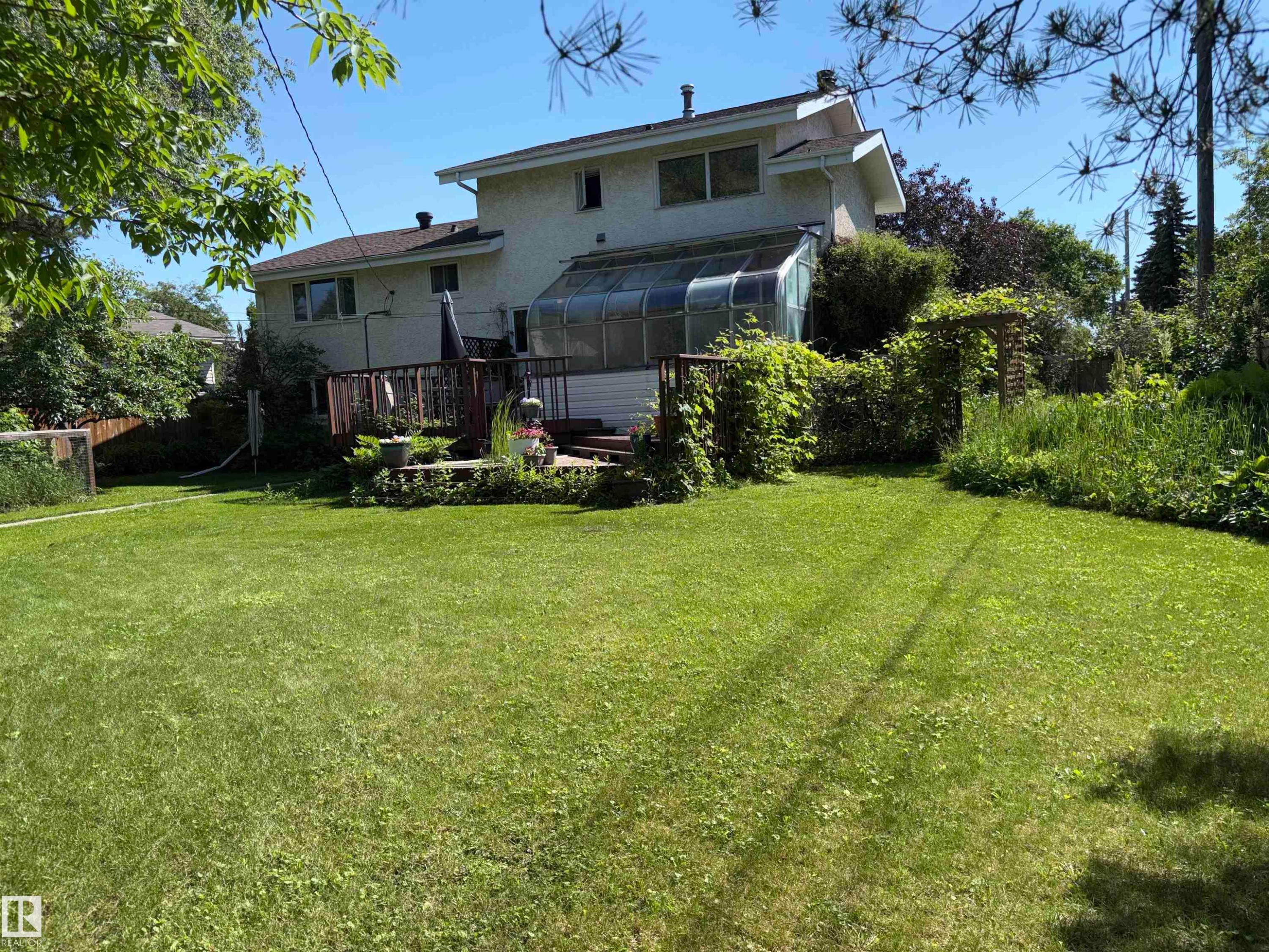 Expansive rear lawn featuring a multi-level wood deck, an attached sunroom, and mature perimeter landscaping - 8812 146 Street, Edmonton, AB