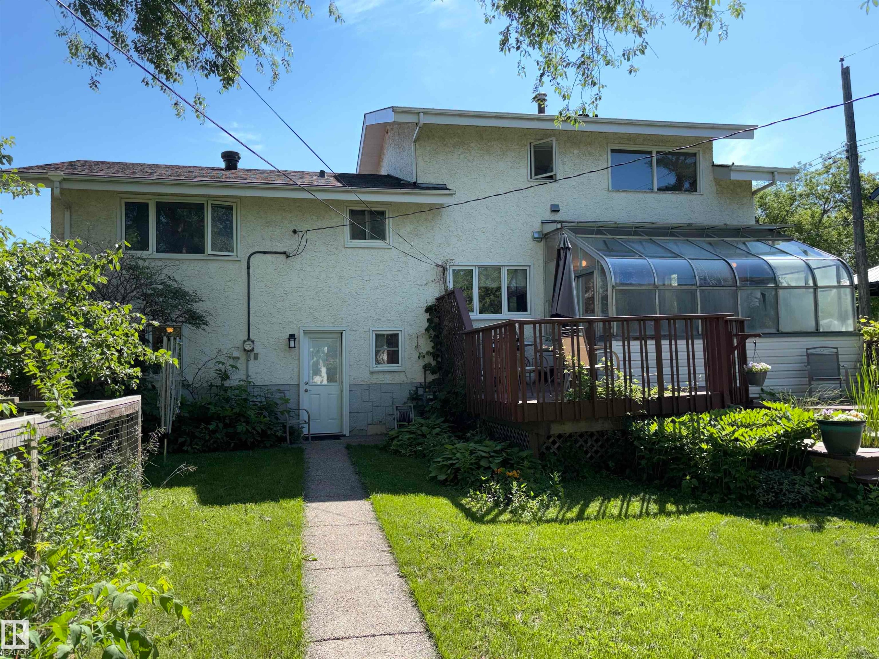 Rear exterior featuring a sunroom addition, wood deck, and stucco siding - 8812 146 Street, Edmonton, AB