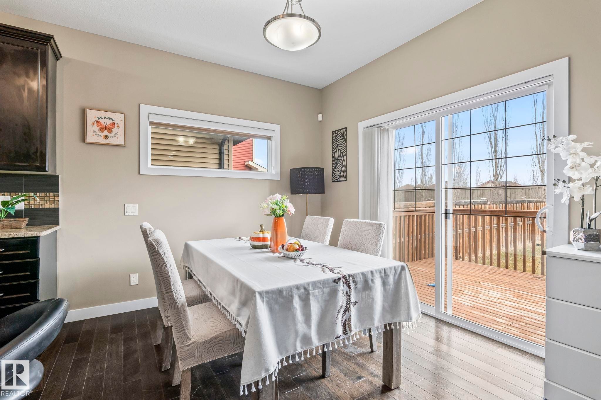 Sliding glass doors opening to an outdoor deck, dark wood-finish flooring, a built-in kitchen cabinet with a granite countertop, mosaic tile backsplash, and a horizontal transom window - 8431 216 St Nw Nw, Edmonton, AB - Indoor Photo Showing Dining Room