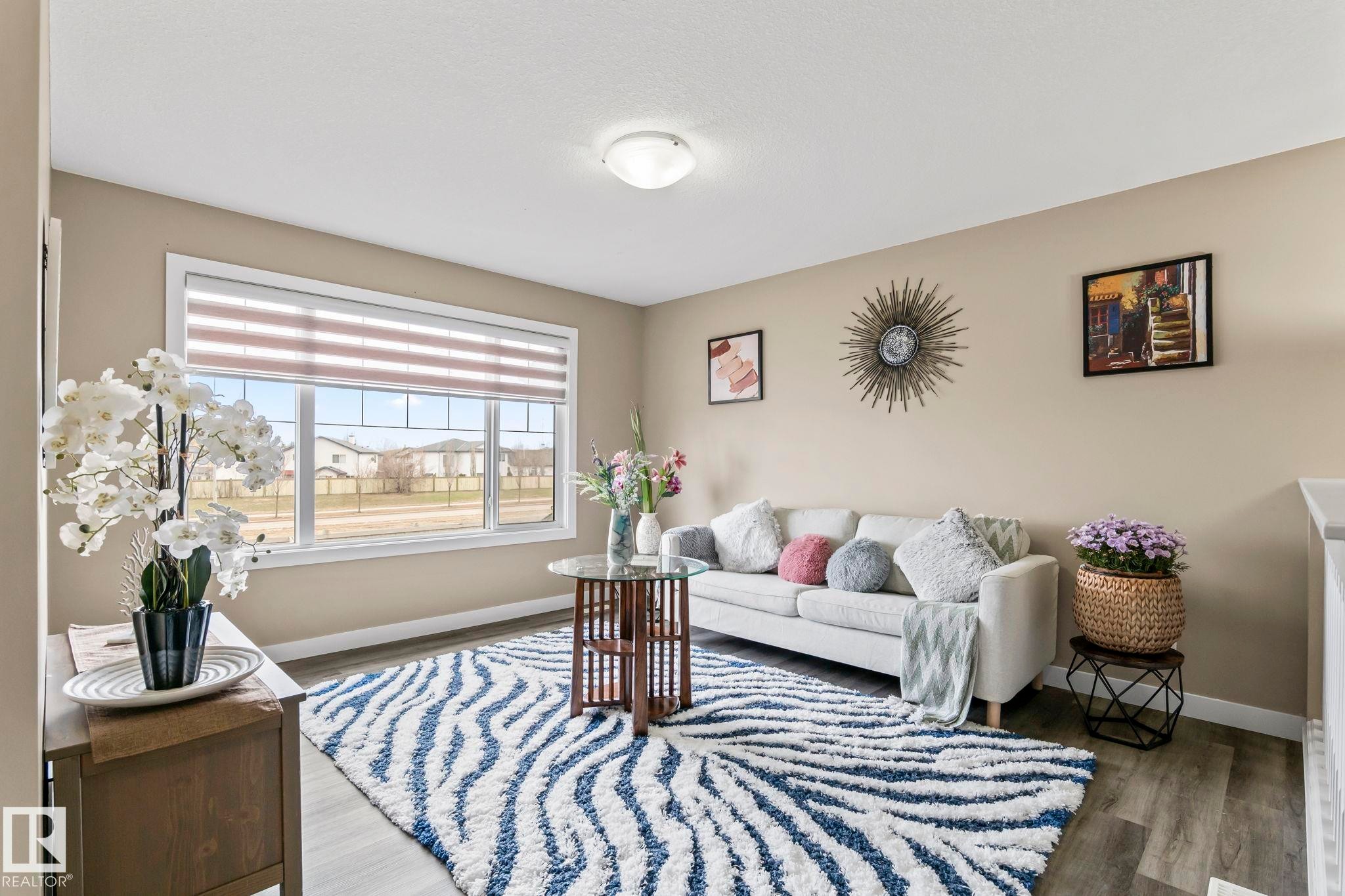 Spacious living area featuring large windows with horizontal blinds, light wood-finish flooring, and neutral wall tones - 8431 216 St Nw Nw, Edmonton, AB - Indoor Photo Showing Other Room