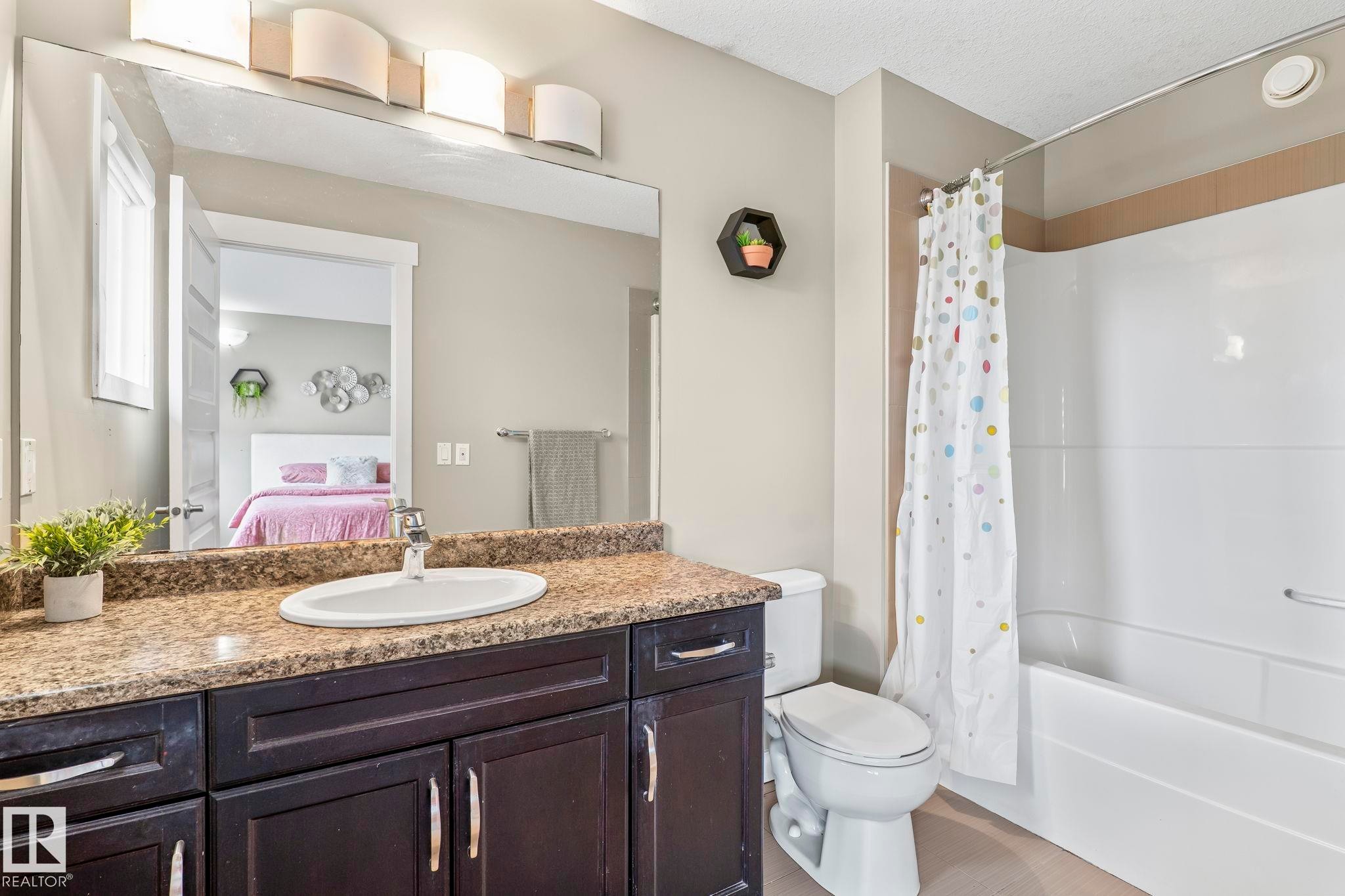 Bathroom featuring a dark wood-finish vanity with a light brown speckled countertop, an undermount sink with a chrome faucet, and a large wall-mounted mirror - 8431 216 St Nw Nw, Edmonton, AB - Indoor Photo Showing Bathroom