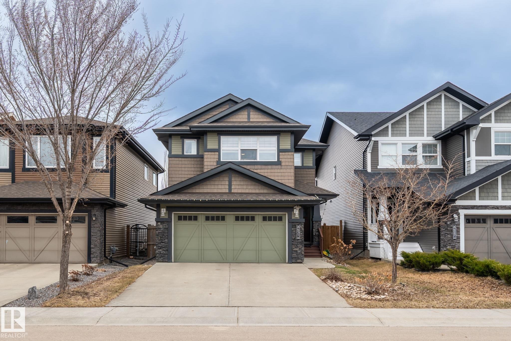 Multi-level home featuring a light green double garage door, stone veneer accents, and dark trim details - 8431 216 St Nw Nw, Edmonton, AB - Outdoor With Facade
