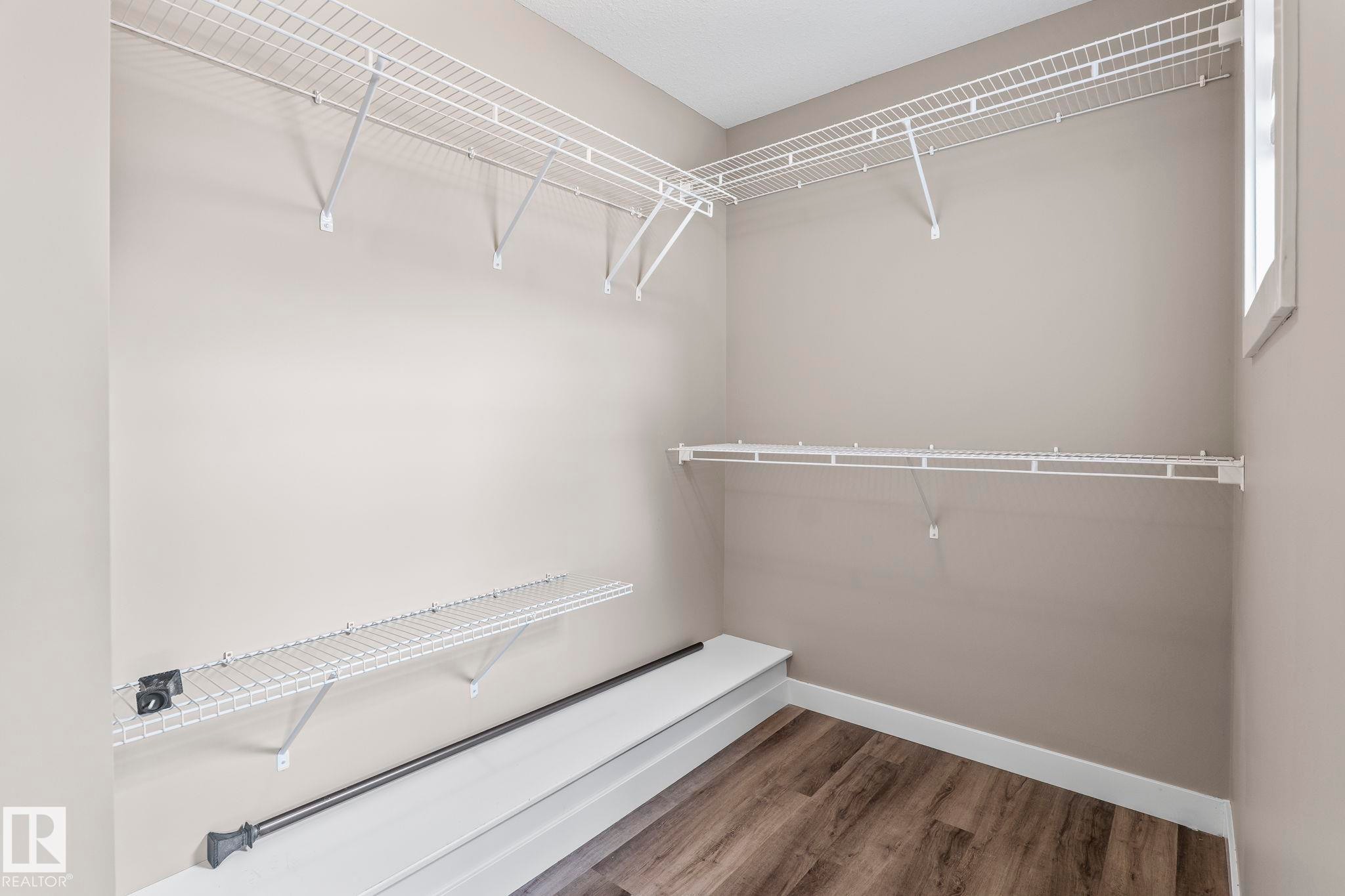 Walk-in closet featuring extensive wire shelving, a clothing rod, wood-finish flooring, light neutral wall paint, and natural light from a window - 8431 216 St Nw Nw, Edmonton, AB - Indoor With Storage