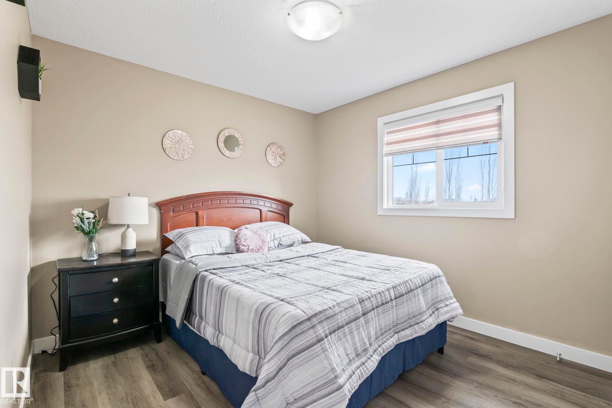 Bedroom featuring wood-finish flooring, a contemporary ceiling light fixture, a window with horizontal blinds, and neutral-toned walls - 8431 216 St Nw Nw, Edmonton, AB - Indoor Photo Showing Bedroom