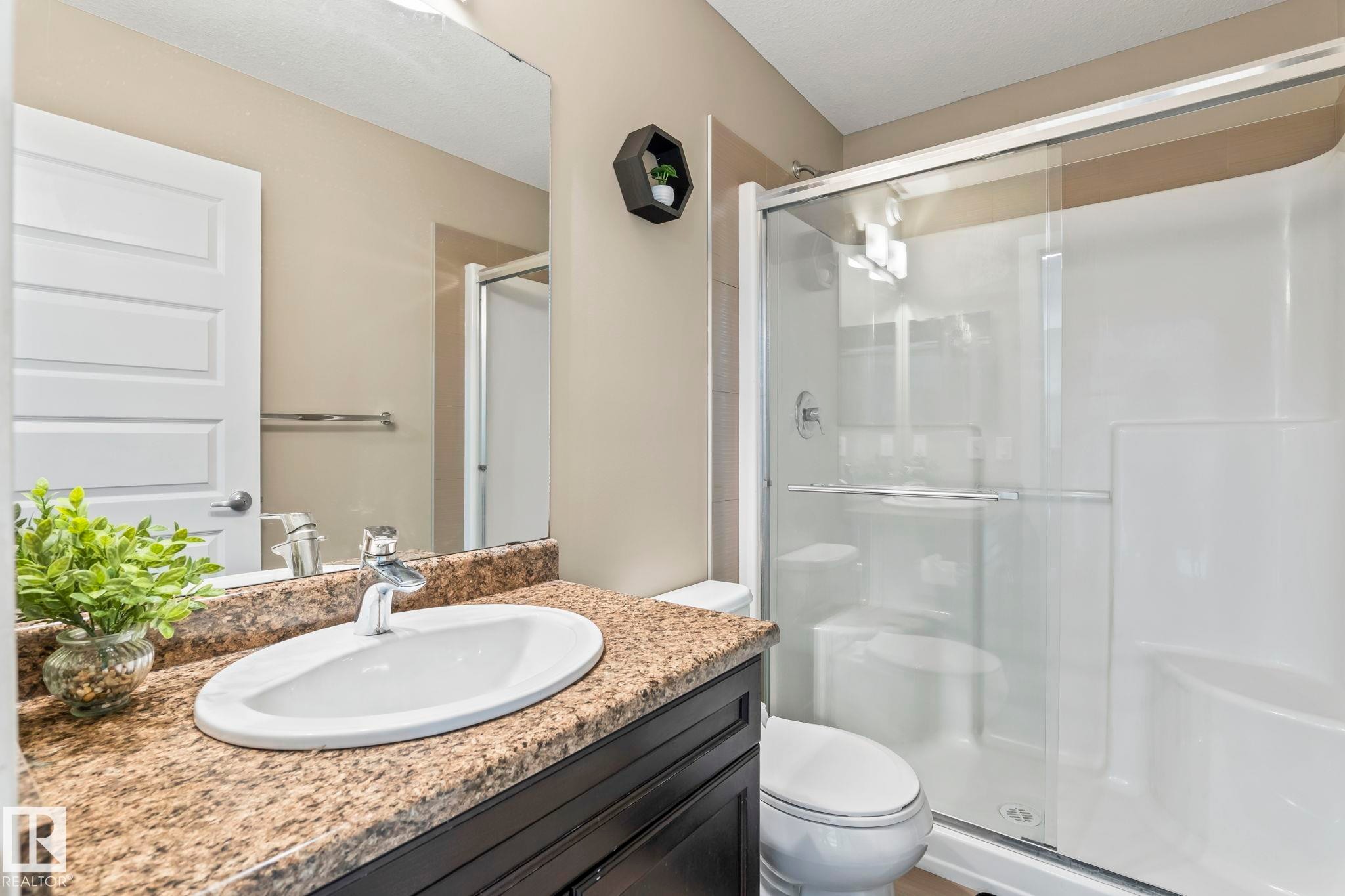 Bathroom featuring a vanity with an oval undermount sink, a granite-look countertop, dark wood-finish cabinetry, a chrome faucet, and a large wall-mounted mirror - 8431 216 St Nw Nw, Edmonton, AB - Indoor Photo Showing Bathroom