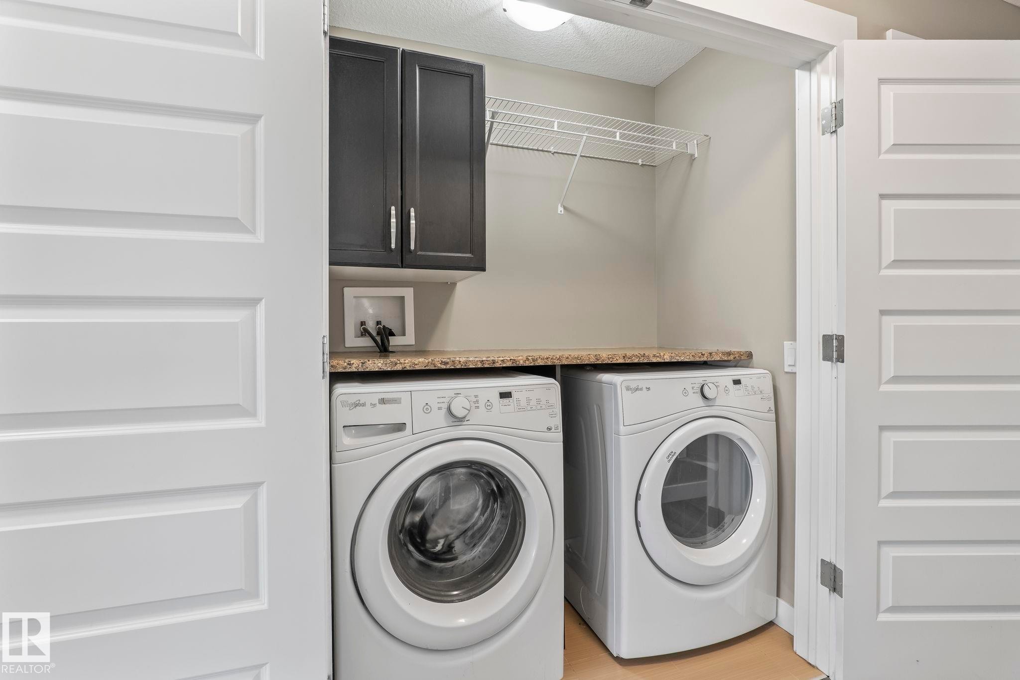 Dedicated laundry area featuring a countertop, dark upper cabinetry, and wire shelving - 8431 216 St Nw Nw, Edmonton, AB - Indoor Photo Showing Laundry Room