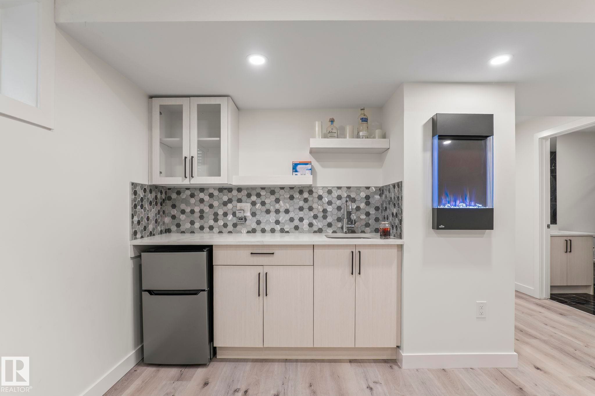 Contemporary kitchenette featuring light wood-finish cabinetry, a built-in sink, and a hexagonal tile backsplash - 8431 216 St Nw Nw, Edmonton, AB - Indoor