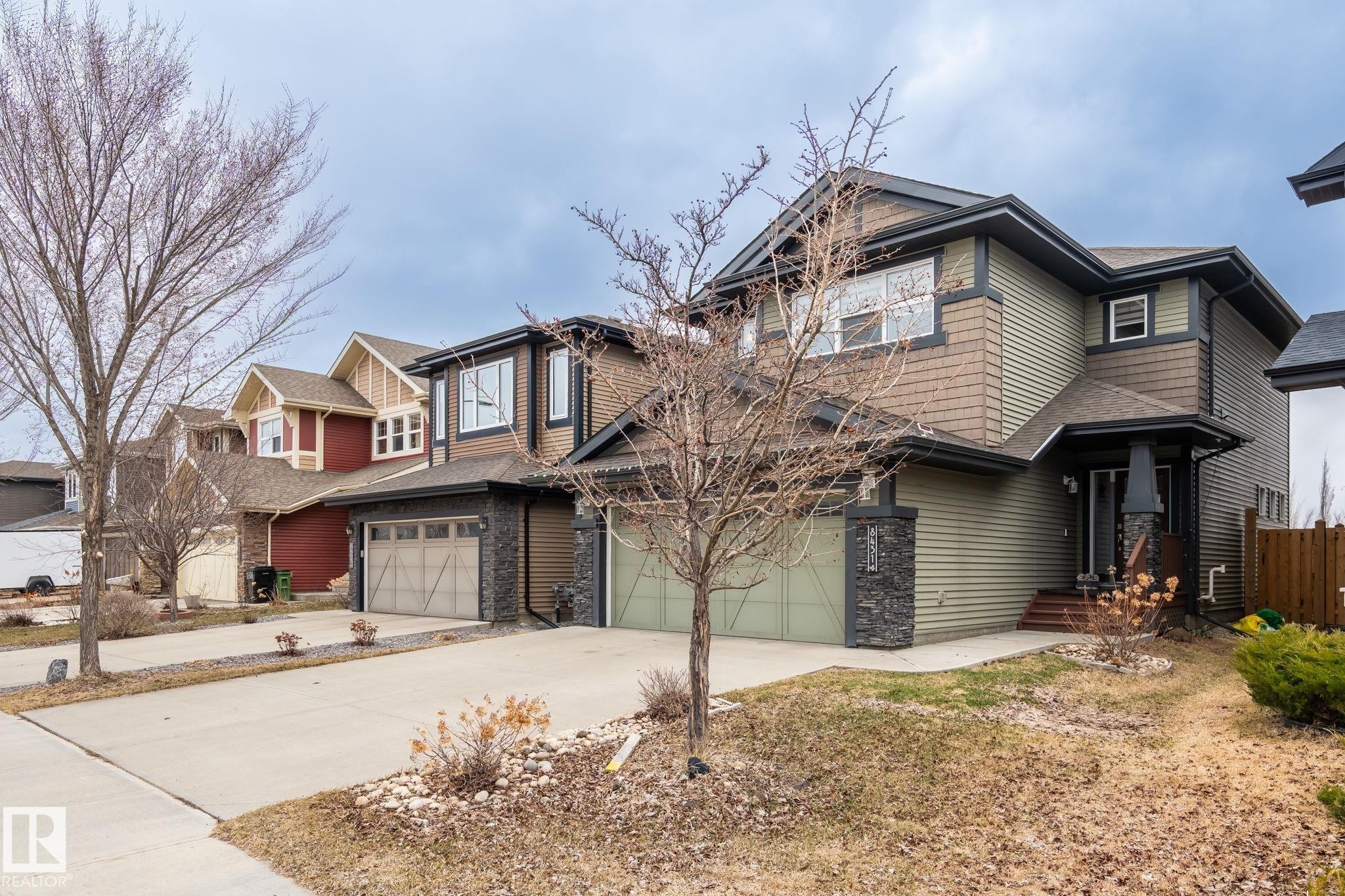 Two-story residence featuring green horizontal siding and brown shake siding, with a stone-clad garage pillar and covered front entry - 8431 216 St Nw Nw, Edmonton, AB - Outdoor With Facade