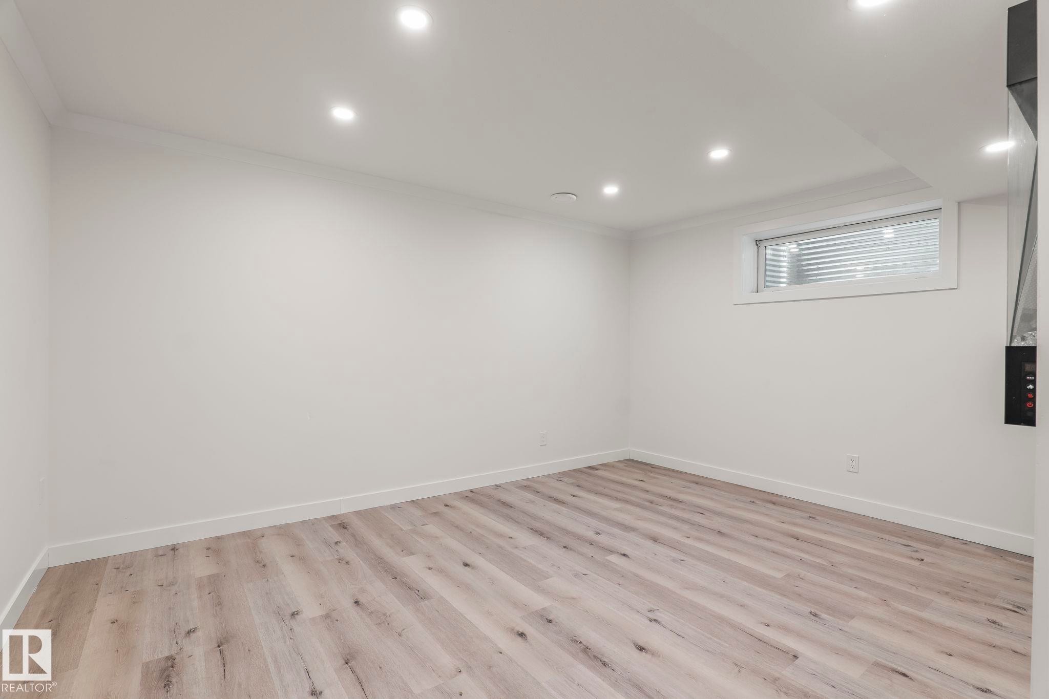 Spacious room featuring wood-finish flooring, recessed ceiling lighting, a window with horizontal blinds, and white baseboards - 8431 216 St Nw Nw, Edmonton, AB - Indoor