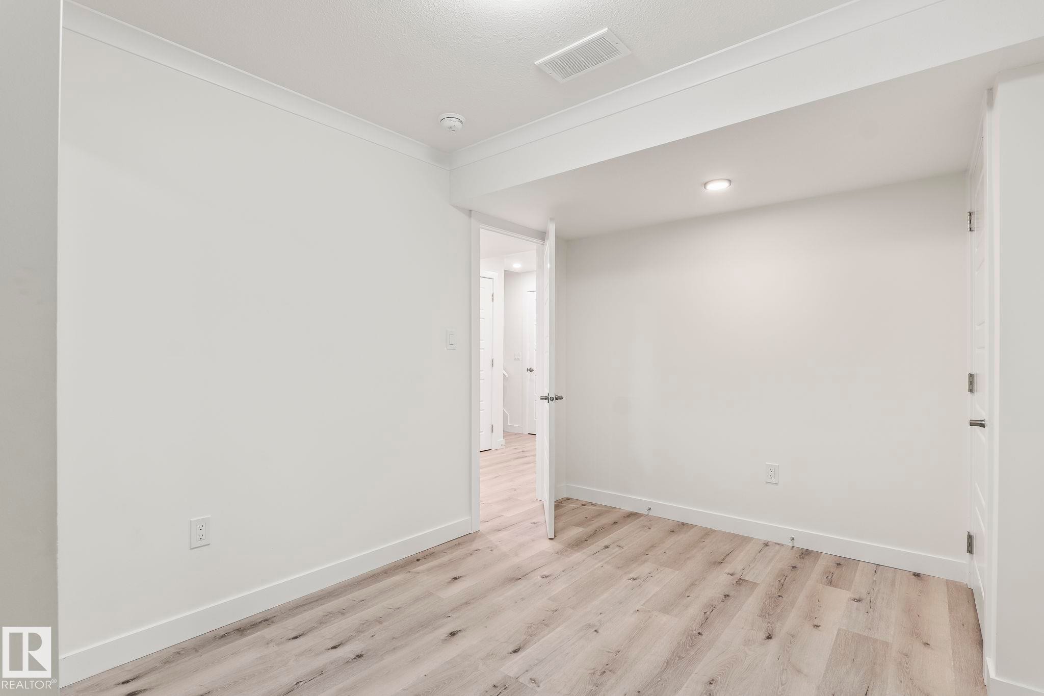 Light wood-finish flooring complements white walls with crown molding and baseboards - 8431 216 St Nw Nw, Edmonton, AB - Indoor Photo Showing Other Room