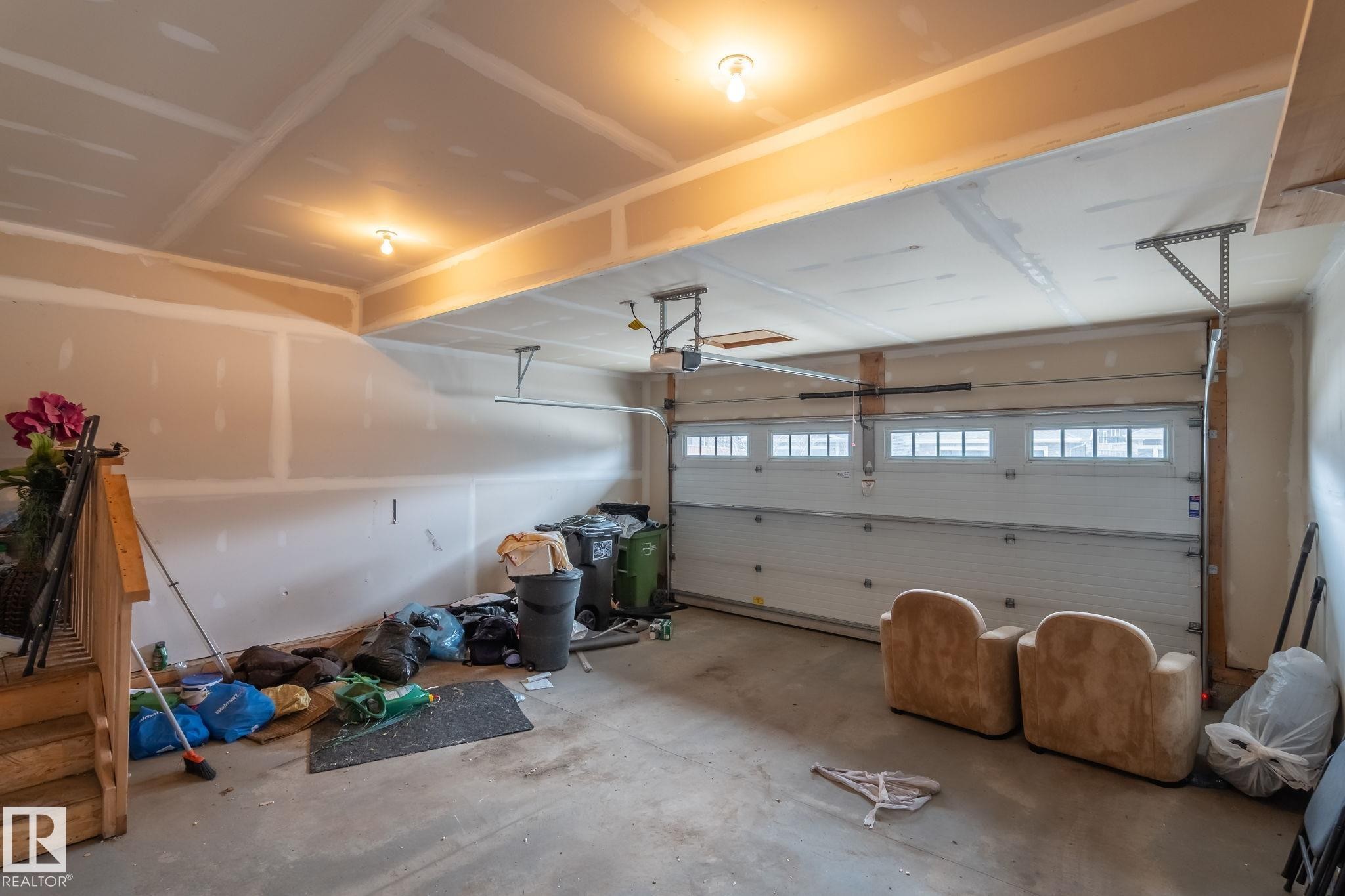 Interior garage space featuring a large overhead door with window inserts, concrete flooring, and exposed ceiling joists - 8431 216 St Nw Nw, Edmonton, AB - Indoor Photo Showing Garage
