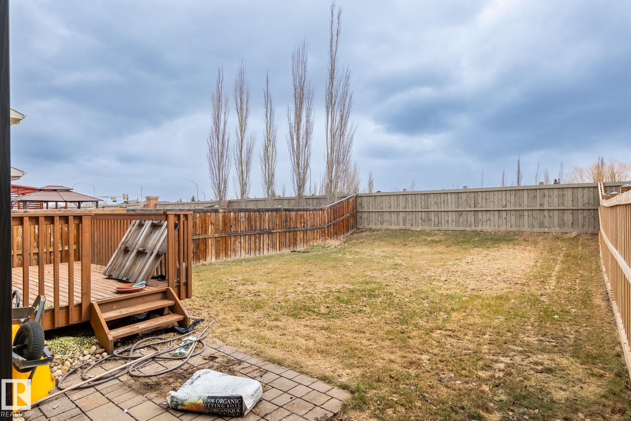 Spacious backyard featuring a wooden deck with railing and stairs, a fully fenced perimeter, and a paver patio area - 8431 216 St Nw Nw, Edmonton, AB - Outdoor