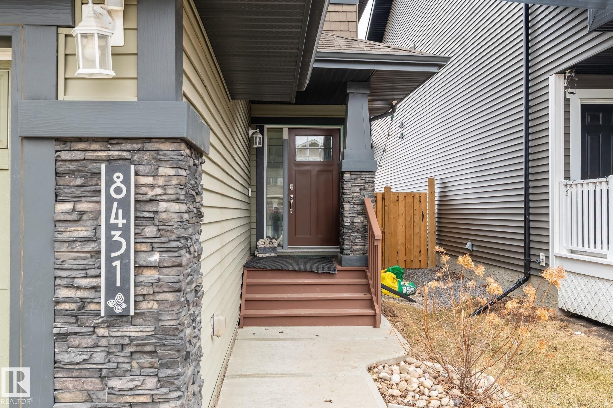 Inviting front entrance featuring a dark wood-finish door with glass panels, a stone veneer pillar, and a concrete pathway - 8431 216 St Nw Nw, Edmonton, AB - Outdoor With Exterior