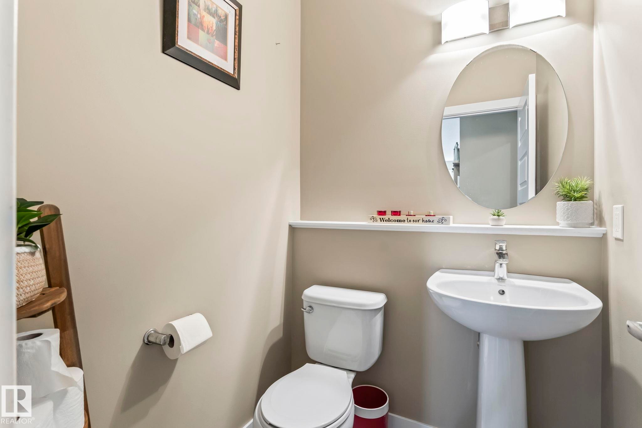Pedestal sink with chrome faucet, oval mirror, and wall-mounted light fixture - 8431 216 St Nw Nw, Edmonton, AB - Indoor Photo Showing Bathroom