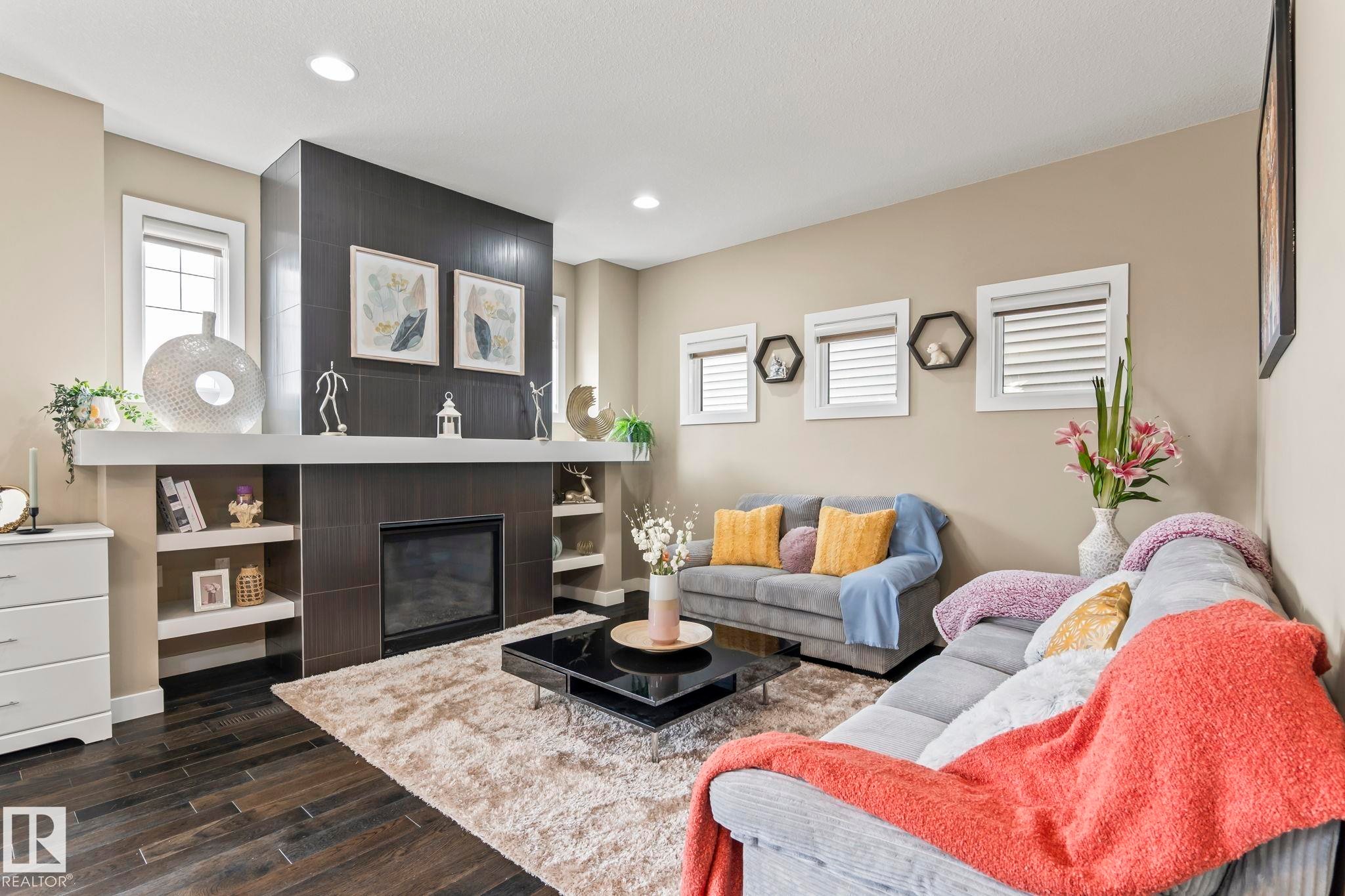 Living area featuring a floor-to-ceiling dark tile fireplace with a white mantel and built-in shelving, wood-finish flooring, recessed lighting, and multiple windows - 8431 216 St Nw Nw, Edmonton, AB - Indoor Photo Showing Living Room With Fireplace