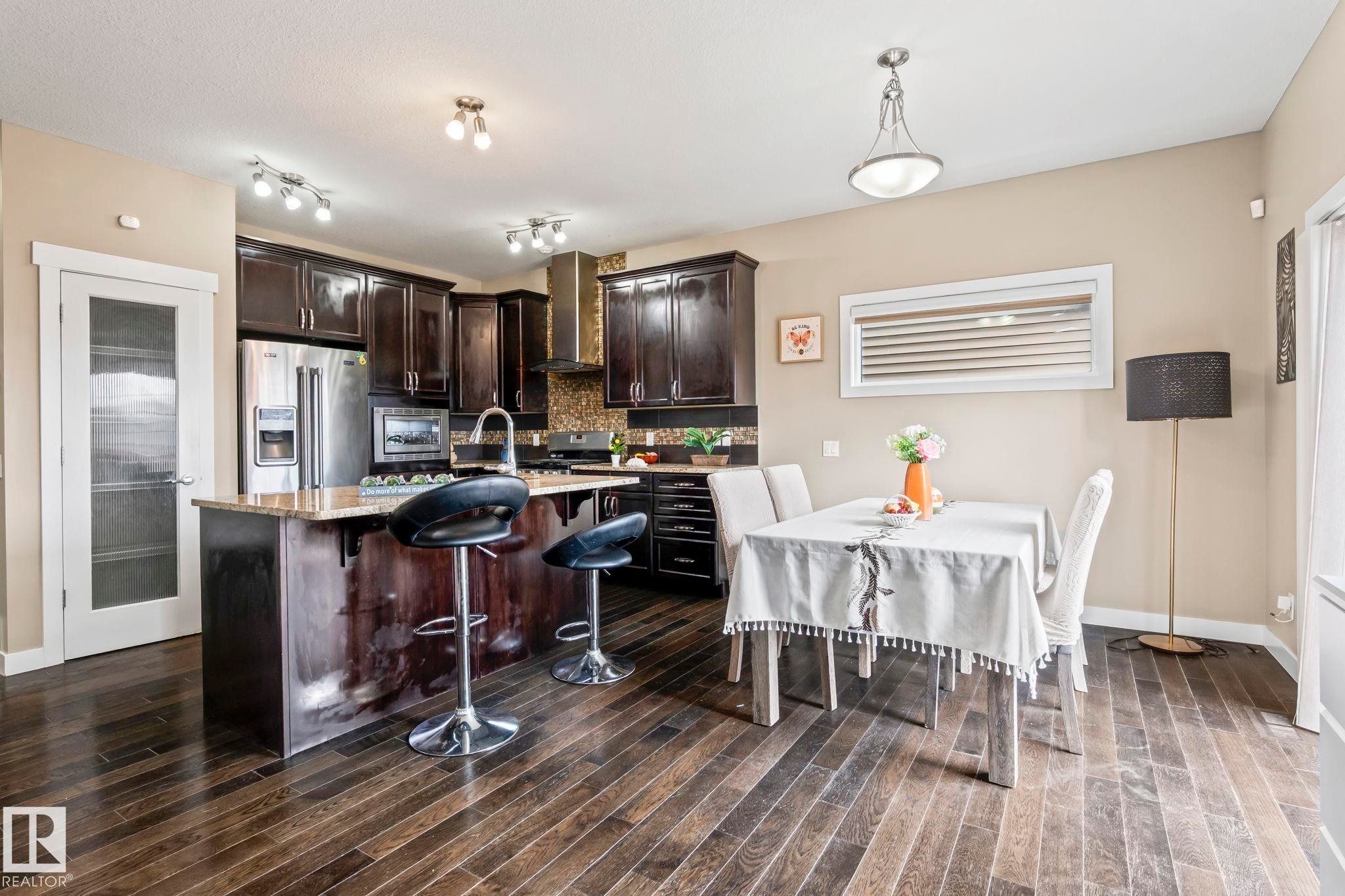 Kitchen featuring dark wood cabinetry, stainless steel appliances, a center island with bar seating, and stone countertops - 8431 216 St Nw Nw, Edmonton, AB - Indoor Photo Showing Other Room