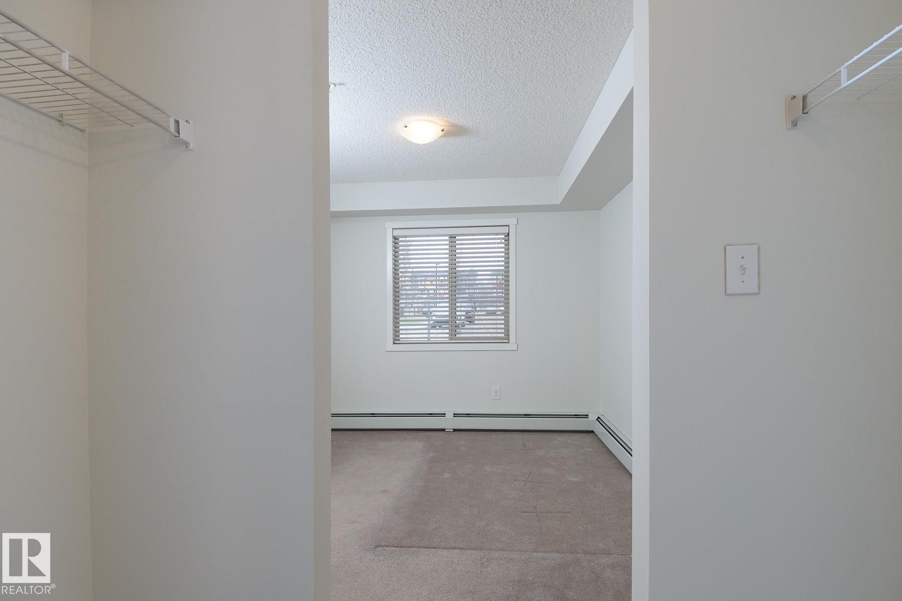 Room featuring soft neutral carpeting, a large window with horizontal blinds, and a built-in wire shelving system - 111 25 Element Dr, St. Albert, AB - Indoor With Storage