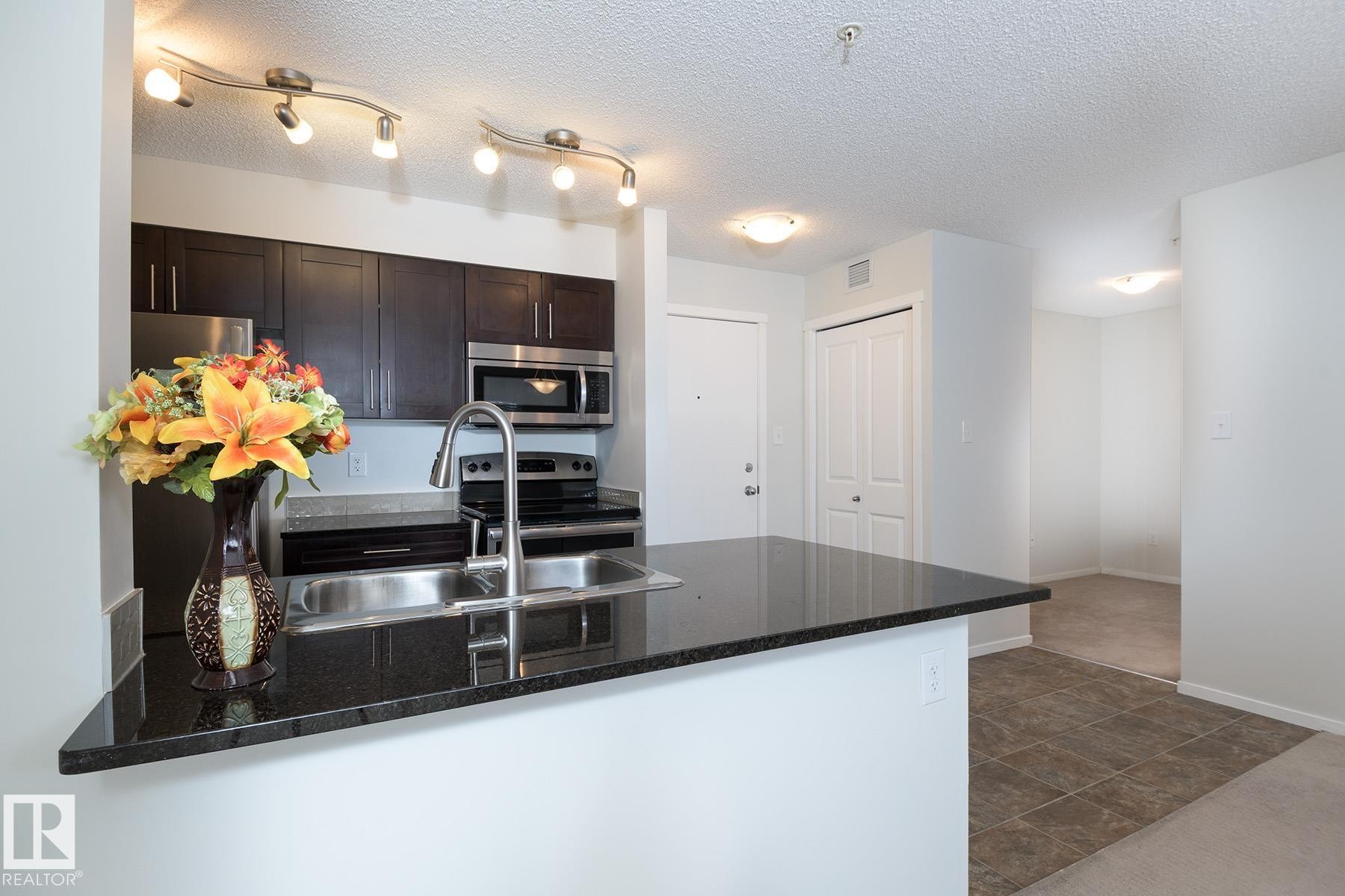 Kitchen featuring dark wood cabinetry, stainless steel appliances, a double basin sink with a high-arc faucet, and granite countertops - 111 25 Element Dr, St. Albert, AB - Indoor Photo Showing Kitchen With Double Sink