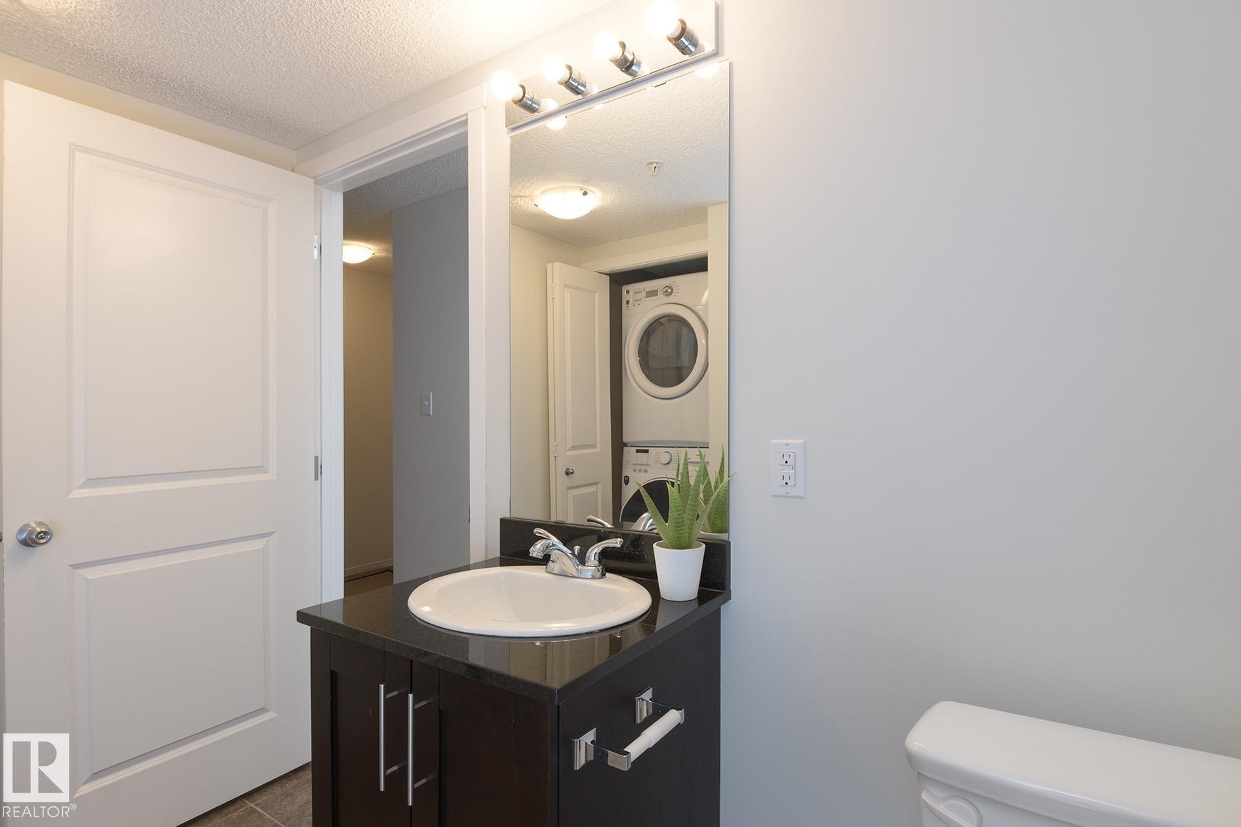 Bathroom vanity with dark wood-finish cabinetry, a black countertop, and an undermount sink - 111 25 Element Dr, St. Albert, AB - Indoor Photo Showing Bathroom