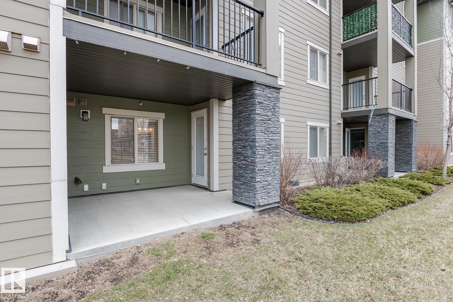 Ground-level patio featuring a concrete surface, a white-framed window with blinds, and a glass-paned door - 111 25 Element Dr, St. Albert, AB - Outdoor With Exterior