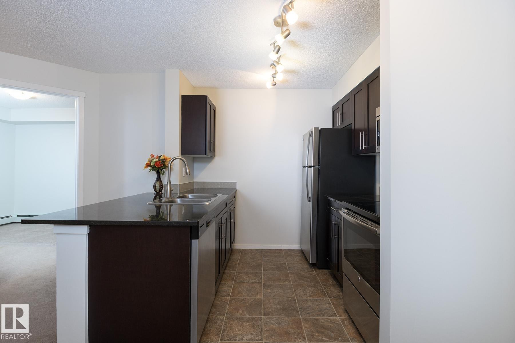 Kitchen featuring dark cabinetry, dark countertops, a stainless steel double sink with a gooseneck faucet, and tile flooring - 111 25 Element Dr, St. Albert, AB - Indoor Photo Showing Kitchen With Double Sink