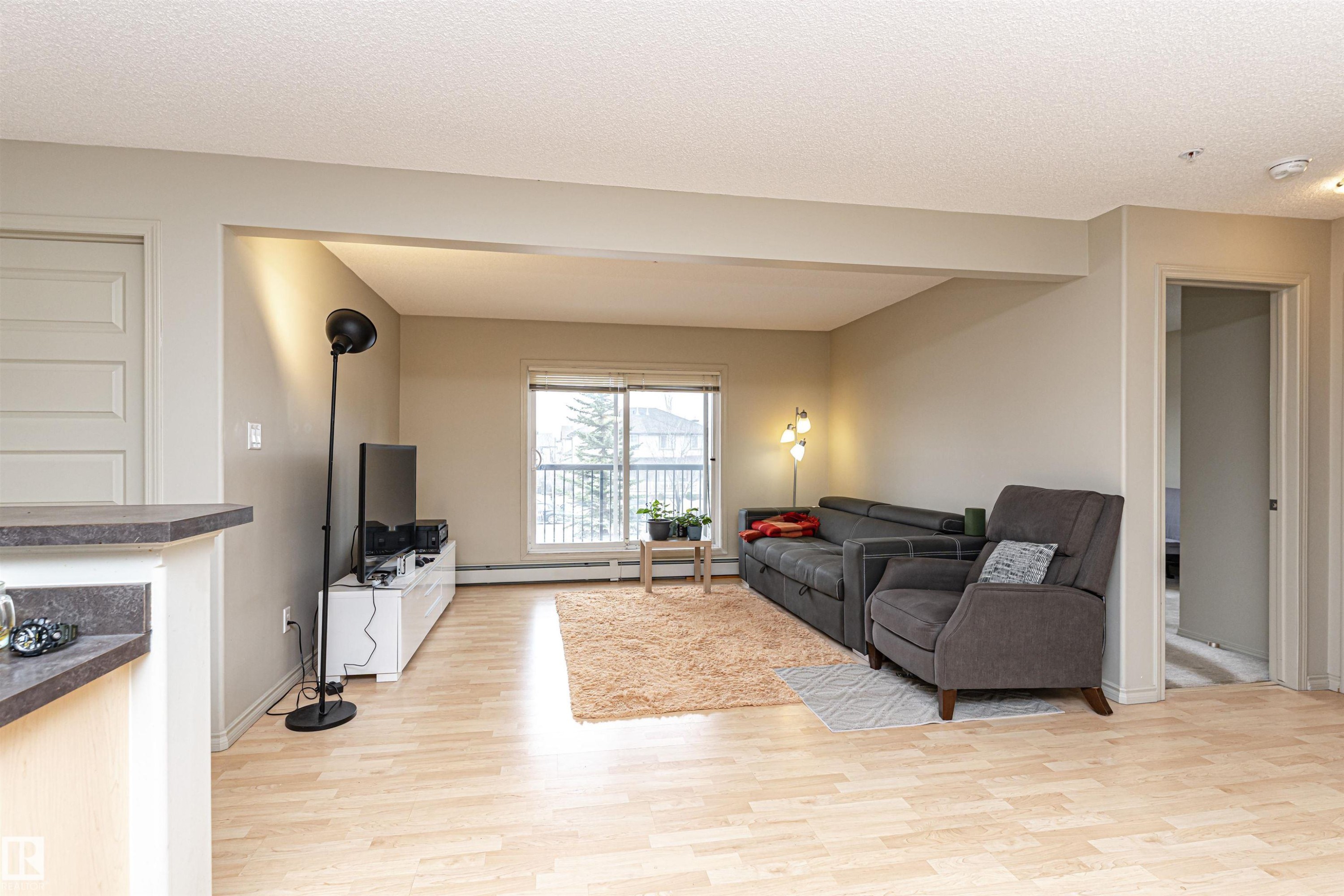 Open-concept living area with light wood-finish flooring, neutral wall tones, and a sliding glass door leading to an outdoor space - 219 646 Mcallister Loop, Edmonton, AB - Indoor Photo Showing Living Room