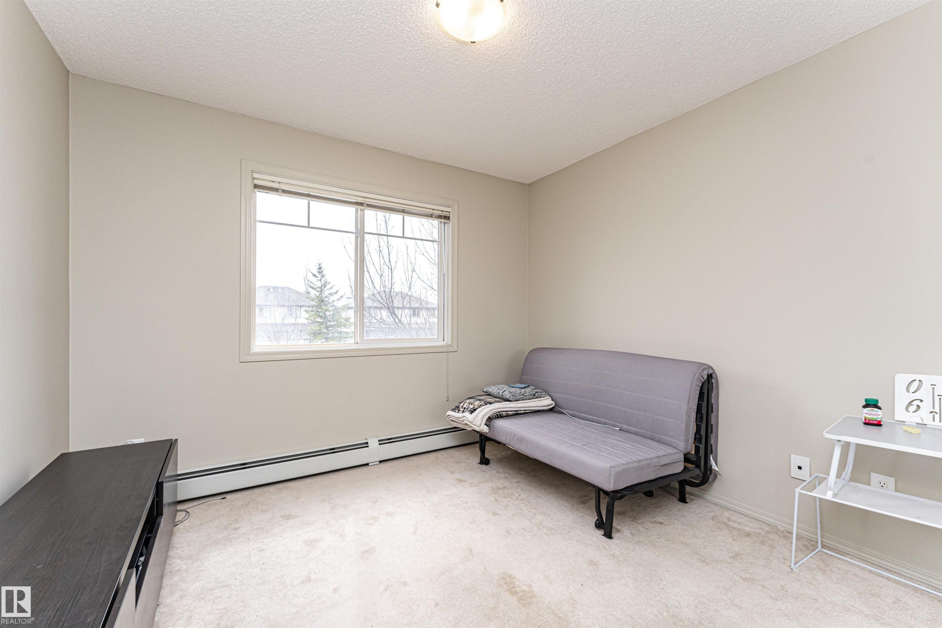 Neutral-toned room featuring a large window with white trim, wall-to-wall carpeting, and baseboard heating - 219 646 Mcallister Loop, Edmonton, AB - Indoor
