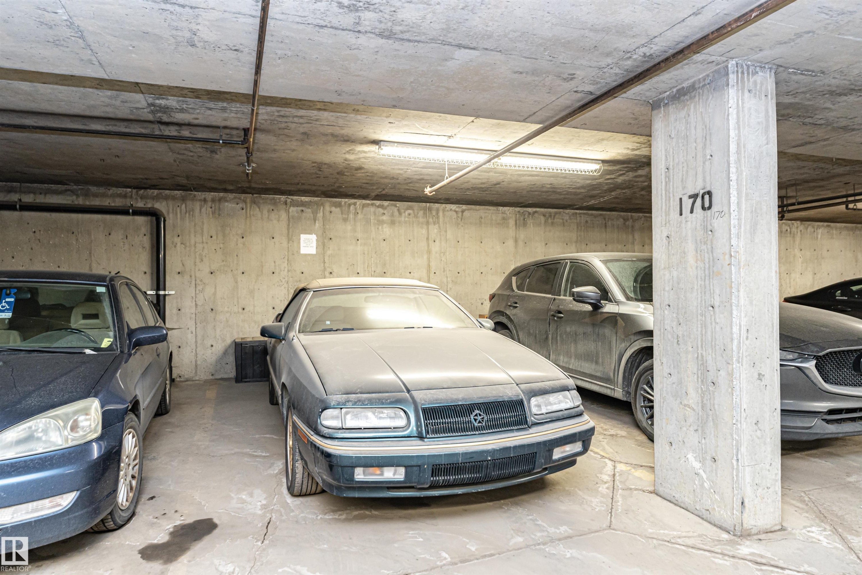 Concrete-finished underground parking space featuring overhead lighting and marked concrete columns - 219 646 Mcallister Loop, Edmonton, AB - Indoor Photo Showing Garage