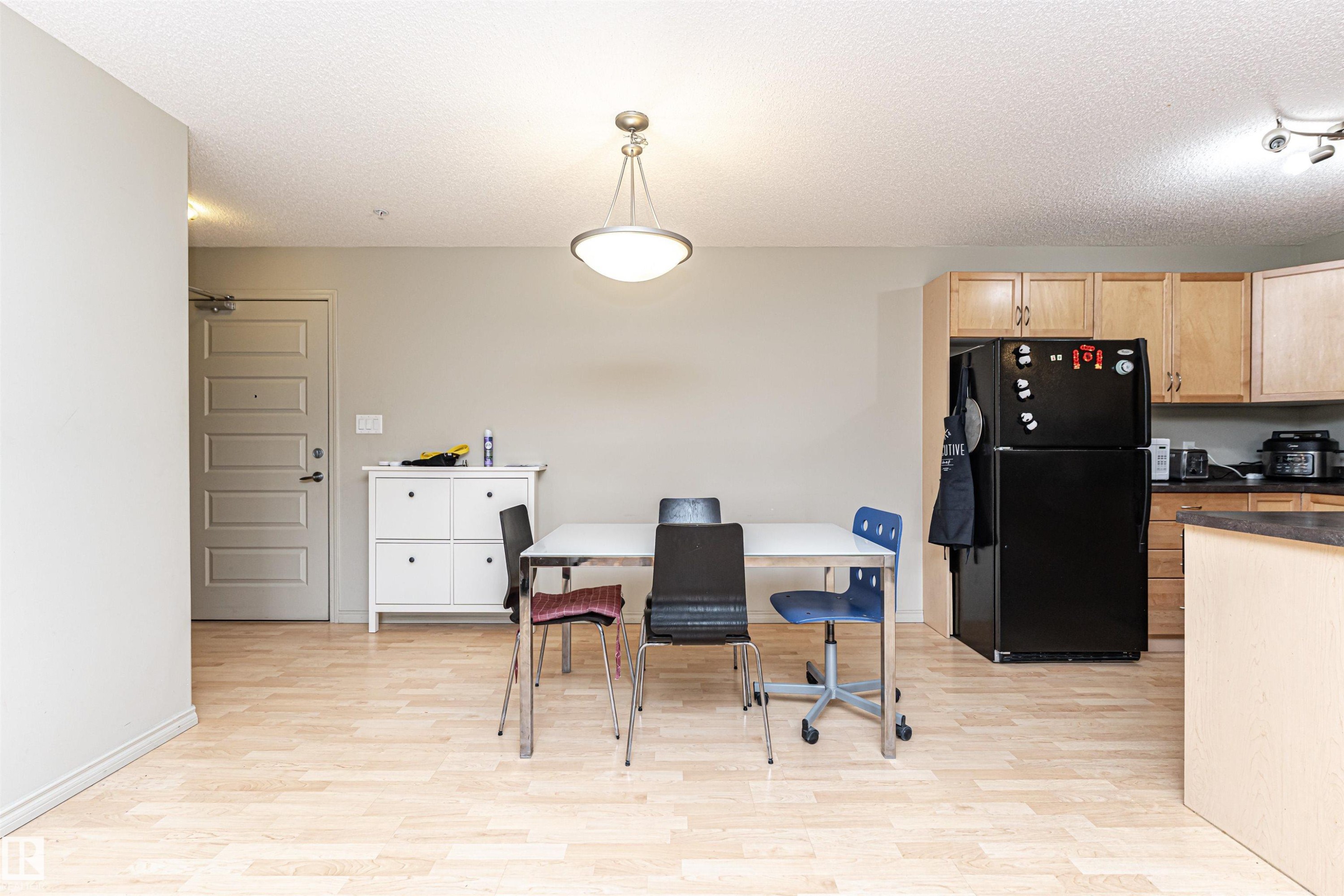 Open-concept living space featuring wood-finish flooring, a contemporary pendant light fixture, and neutral wall tones - 219 646 Mcallister Loop, Edmonton, AB - Indoor Photo Showing Kitchen