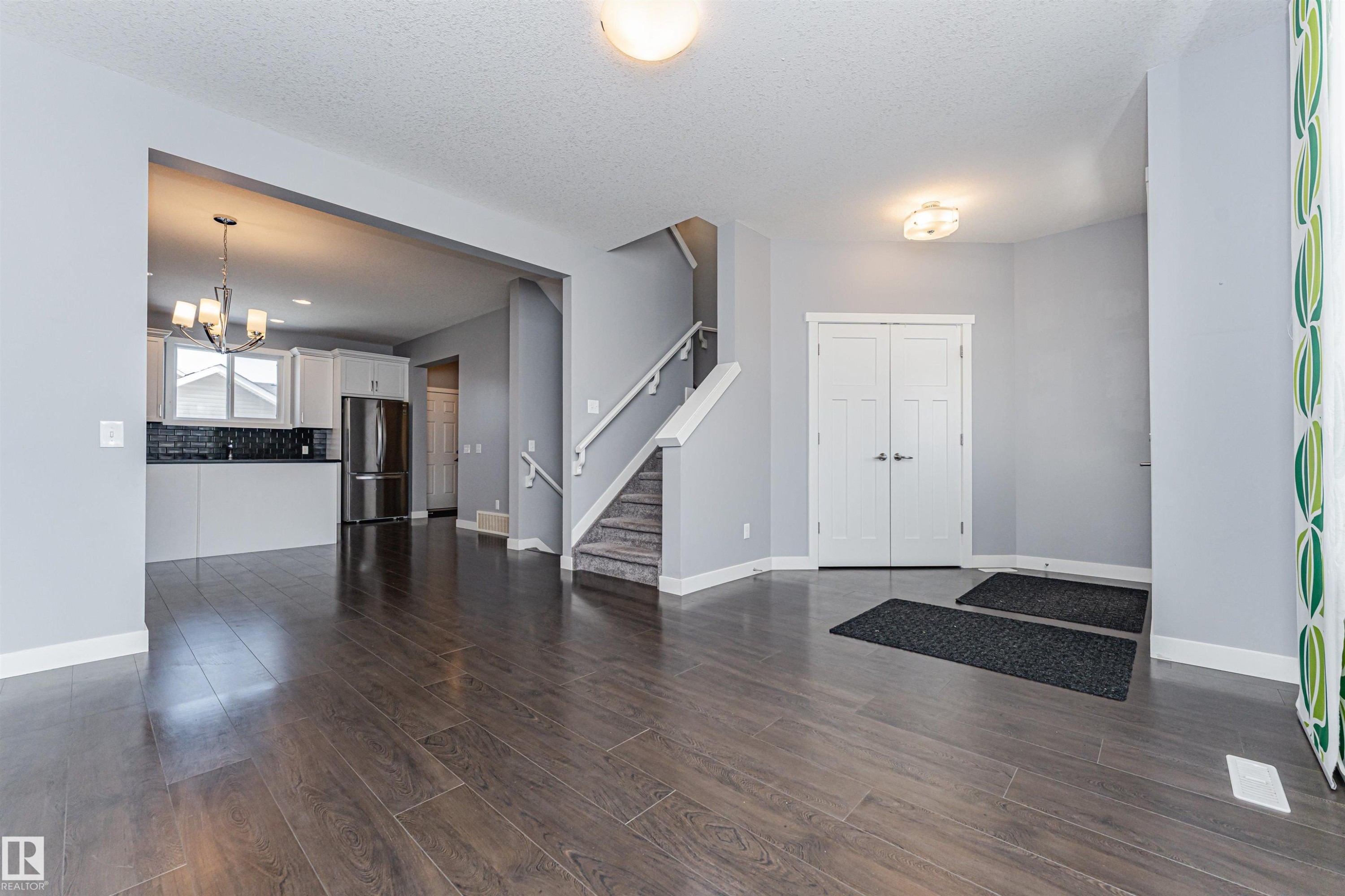 Spacious open-concept living area featuring wood-finish flooring, a kitchen with light cabinetry and stainless steel appliances, and a staircase with white railings - 16420 15 Avenue, Edmonton, AB - Indoor Photo Showing Other Room
