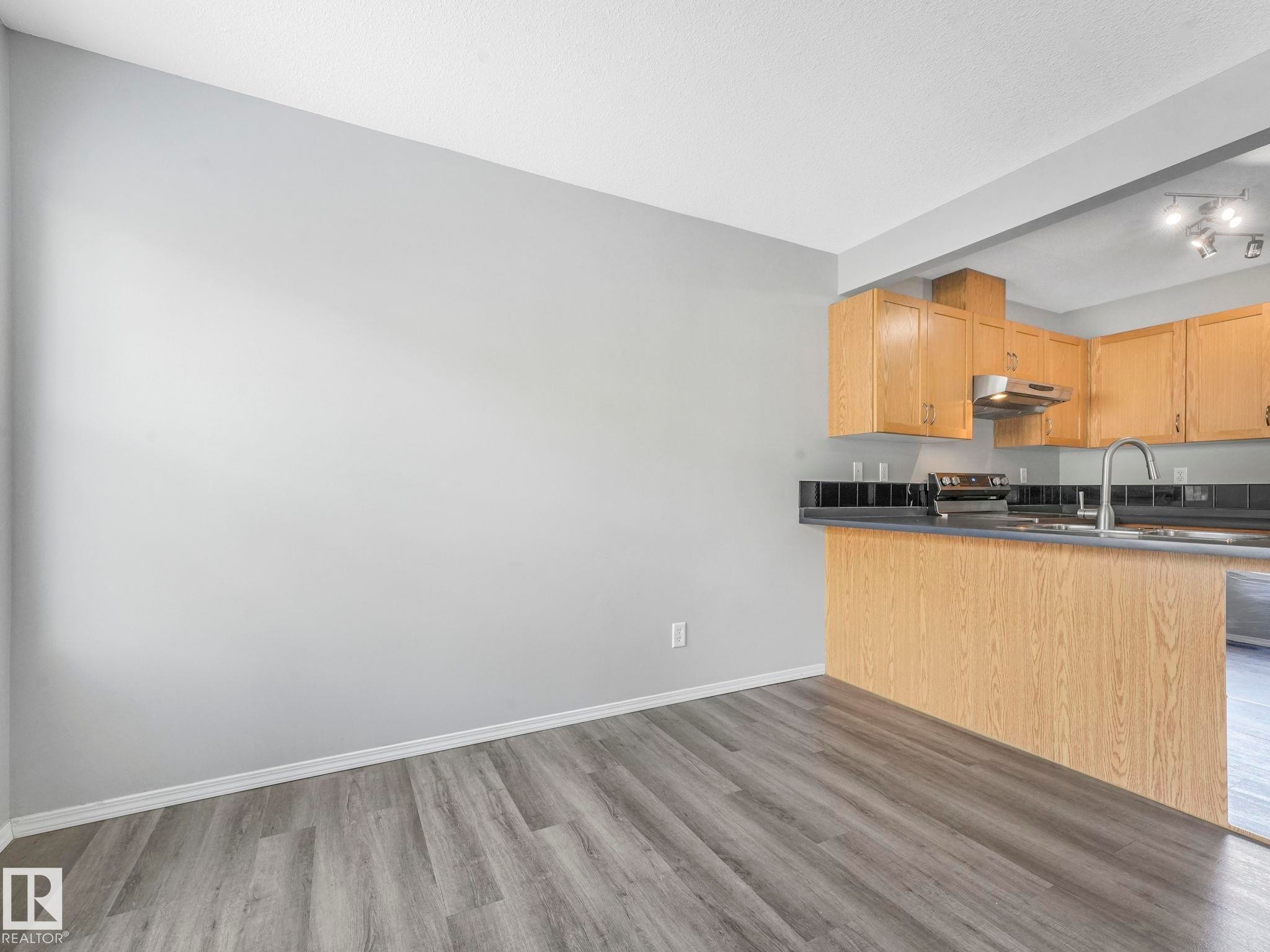 This kitchen features light wood cabinetry, a stainless steel range hood, and a dual basin sink with a chrome faucet - 175 150 Edwards Drive, Edmonton, AB - Indoor Photo Showing Kitchen With Double Sink