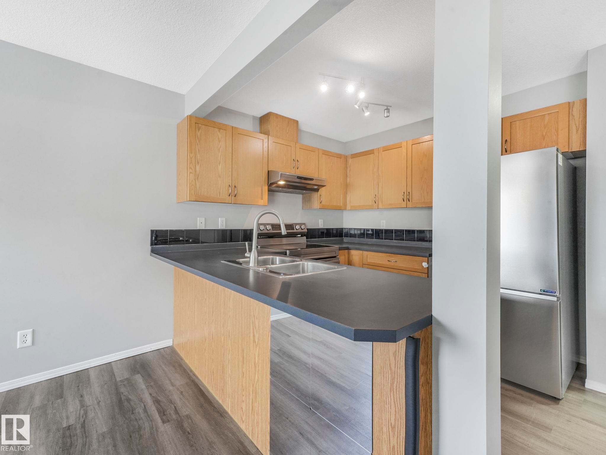 The kitchen features light wood cabinetry, dark countertops, and a stainless steel refrigerator - 175 150 Edwards Drive, Edmonton, AB - Indoor Photo Showing Kitchen With Double Sink