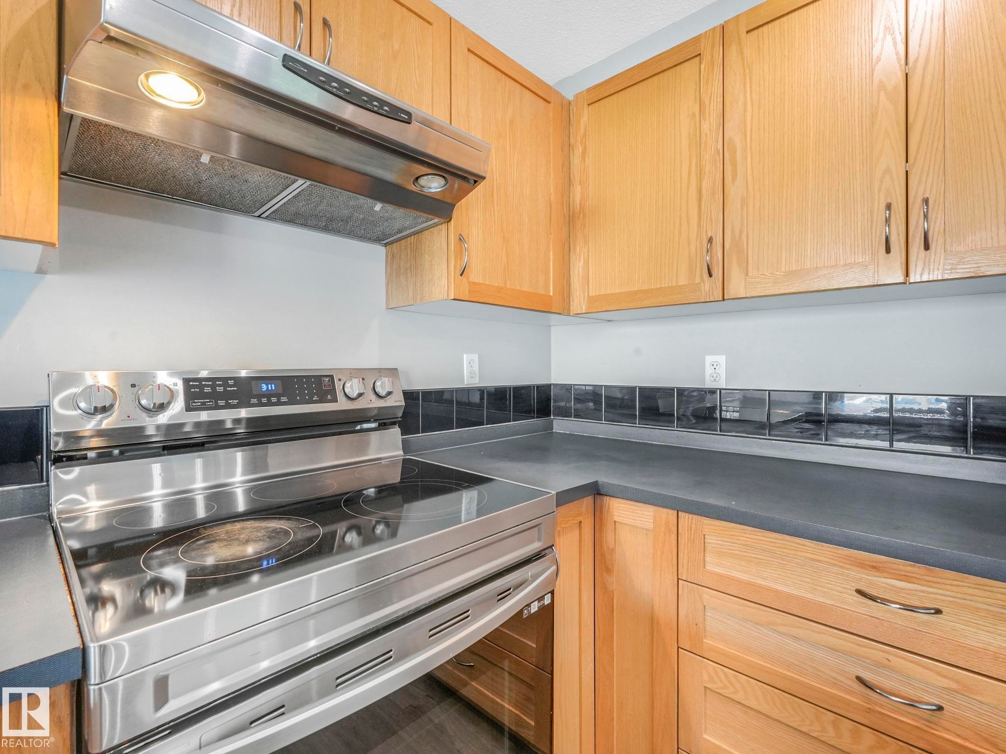 The kitchen features wood cabinetry, a stainless steel range with a smooth cooktop, and a matching stainless steel range hood - 175 150 Edwards Drive, Edmonton, AB - Indoor Photo Showing Kitchen