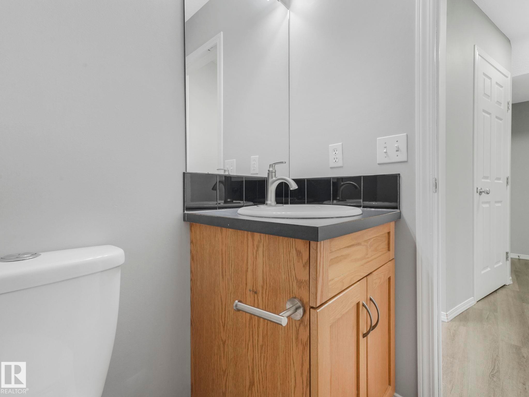 Bathroom vanity with a white oval sink, brushed nickel faucet, wood cabinetry, and a dark countertop - 175 150 Edwards Drive, Edmonton, AB - Indoor Photo Showing Bathroom