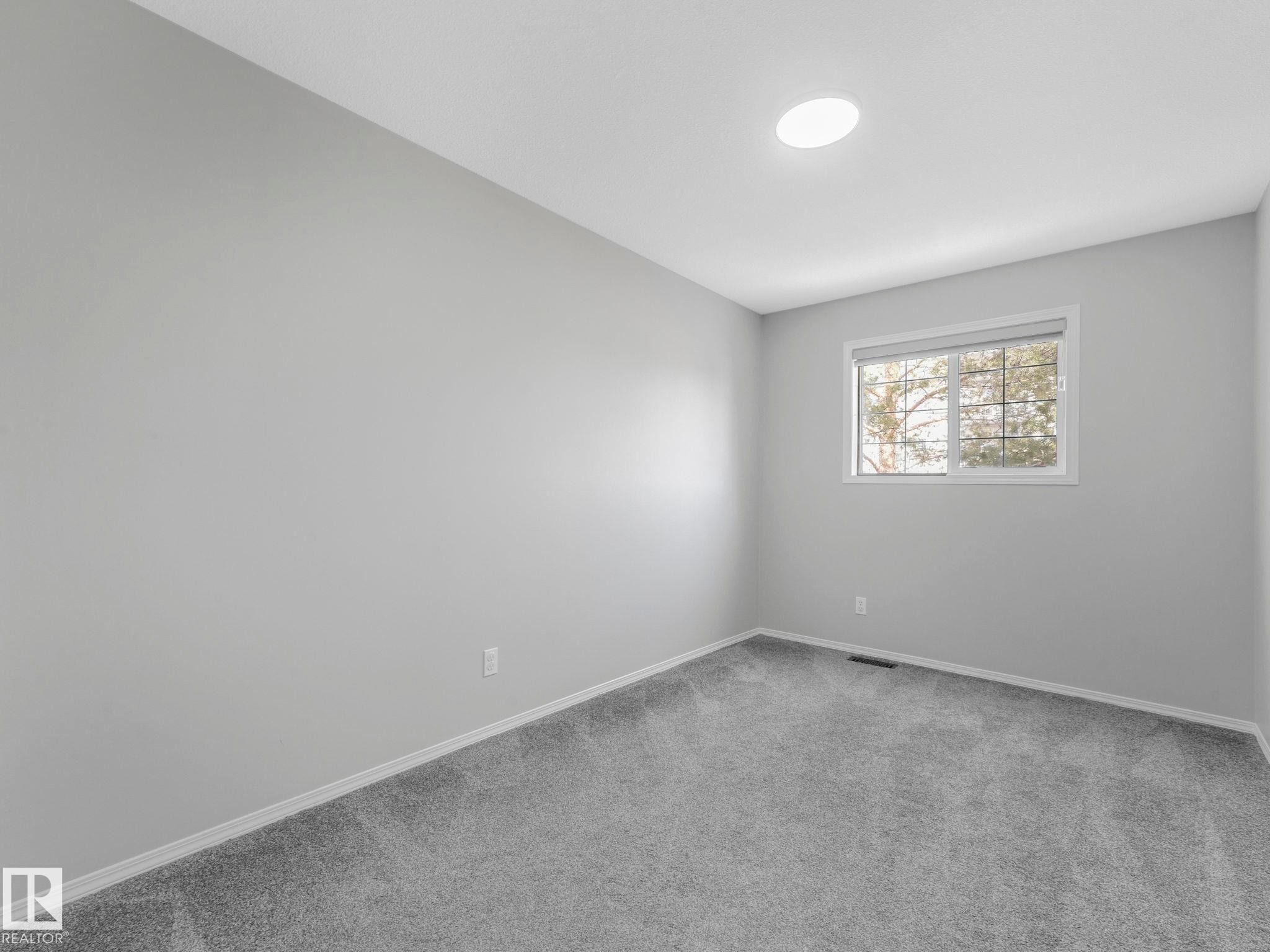 This room features light grey carpeting, white trim, and a window with a view of trees - 175 150 Edwards Drive, Edmonton, AB - Indoor Photo Showing Other Room