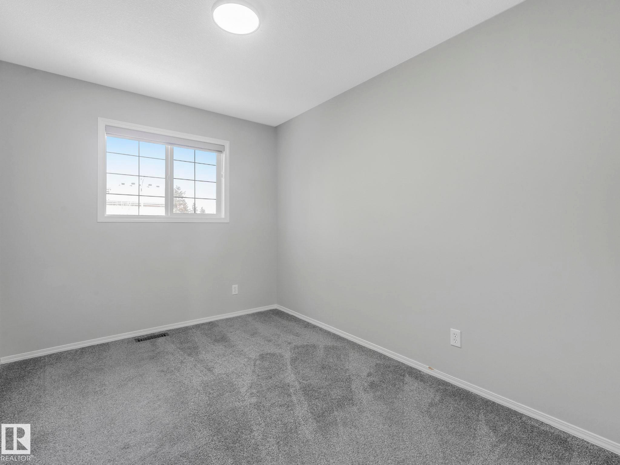 This room features gray carpet flooring, light gray walls, and a window with white framing and grilles - 175 150 Edwards Drive, Edmonton, AB - Indoor Photo Showing Other Room
