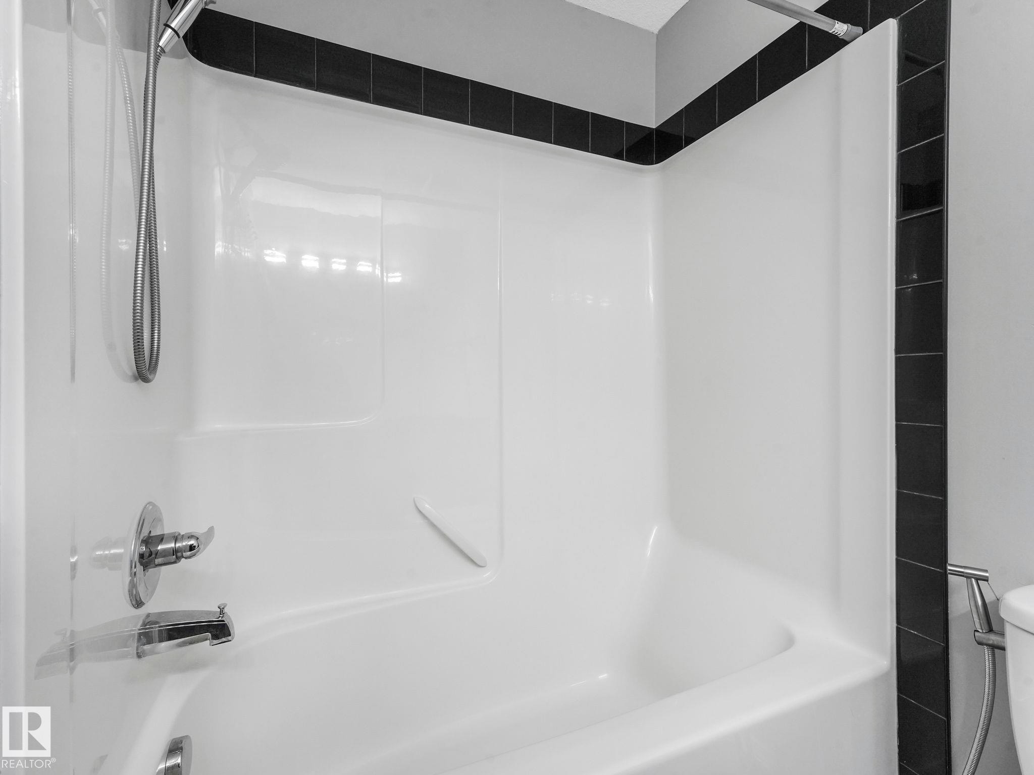 Bathroom featuring a white bathtub with a chrome faucet and shower head, complemented by a black tiled surround - 175 150 Edwards Drive, Edmonton, AB - Indoor Photo Showing Bathroom