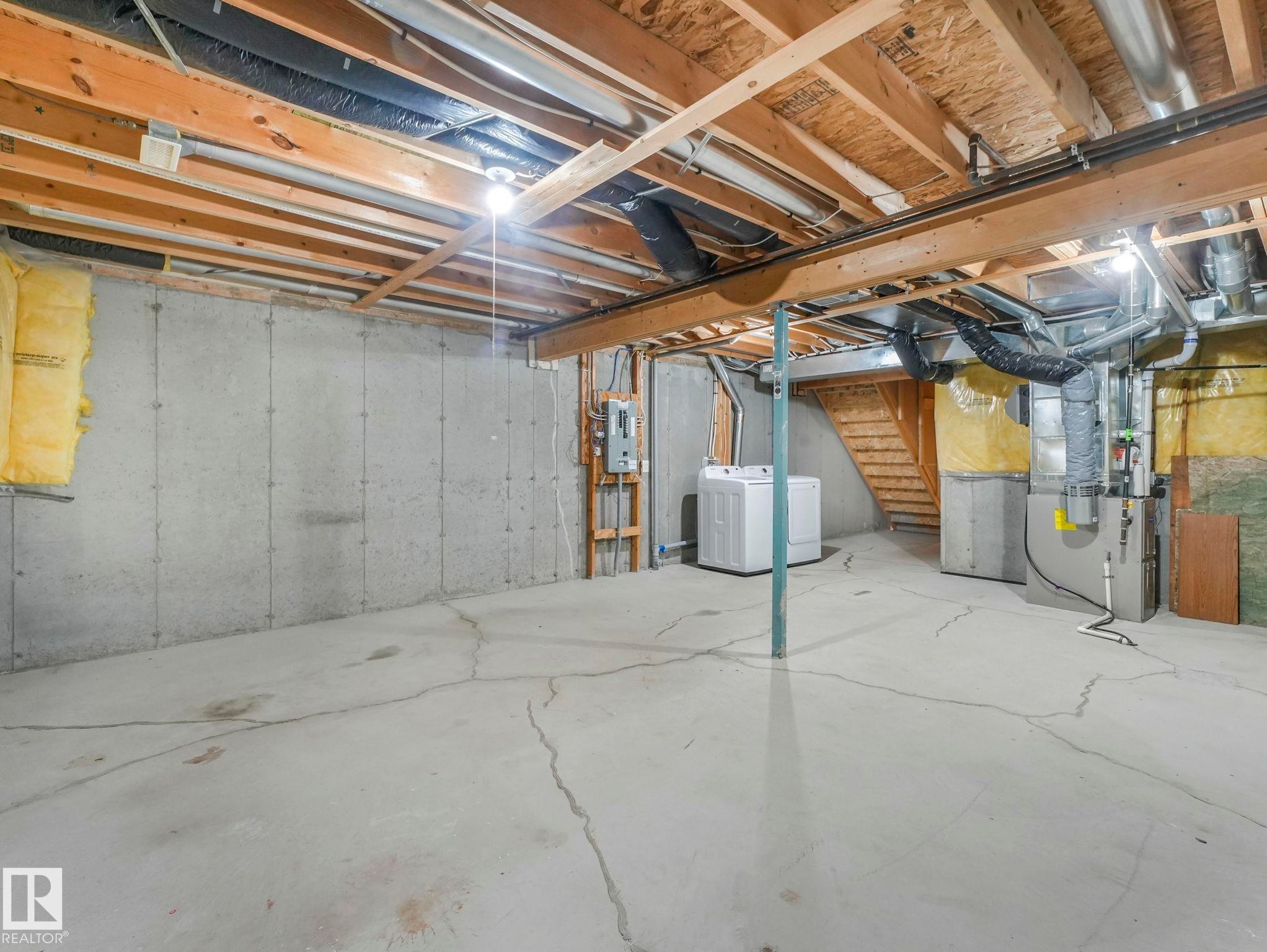The property features an unfinished basement with concrete walls and flooring, exposed ceiling joists, and a utility area with a washing machine and furnace - 175 150 Edwards Drive, Edmonton, AB - Indoor Photo Showing Basement