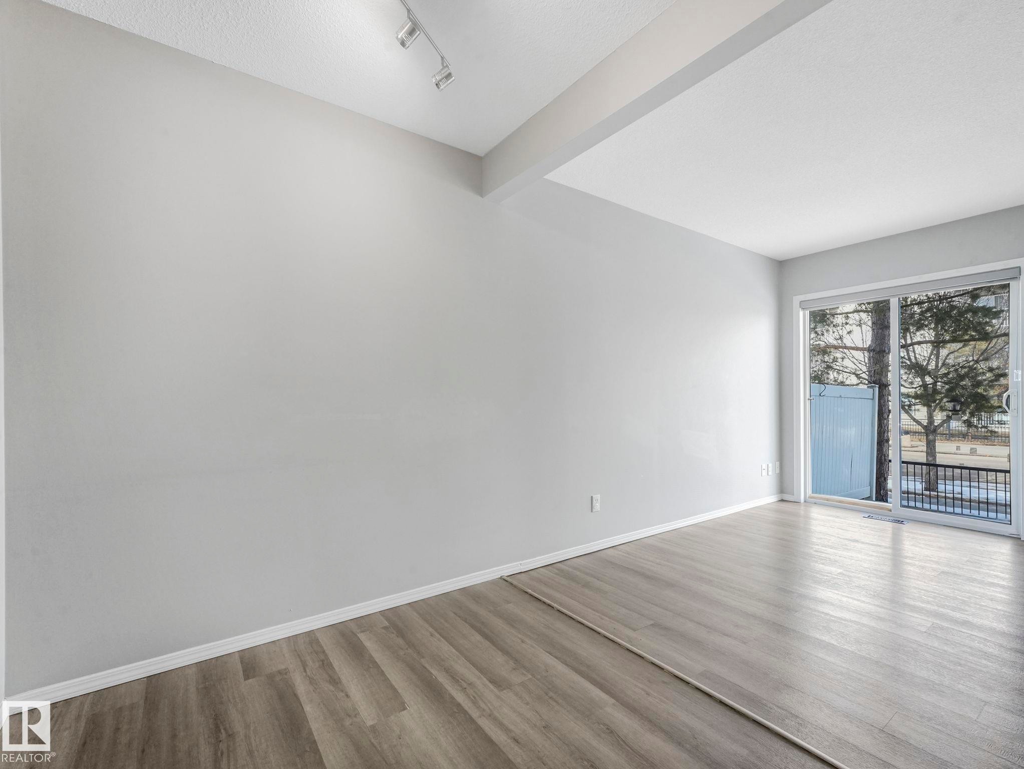Living area featuring light-colored walls, wood-style flooring, track lighting, and a large sliding glass door - 175 150 Edwards Drive, Edmonton, AB - Indoor Photo Showing Other Room