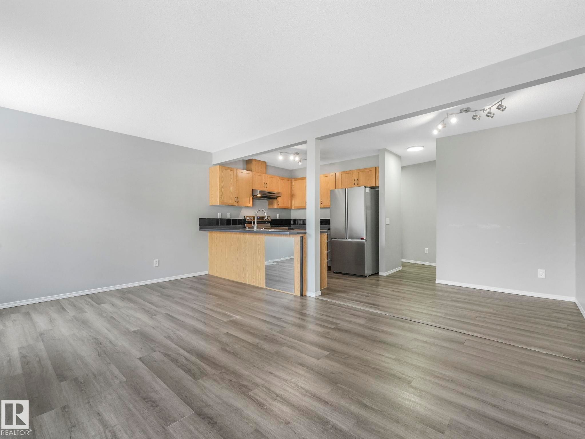 The property features an open living space with gray wood-style flooring and light gray walls - 175 150 Edwards Drive, Edmonton, AB - Indoor Photo Showing Kitchen