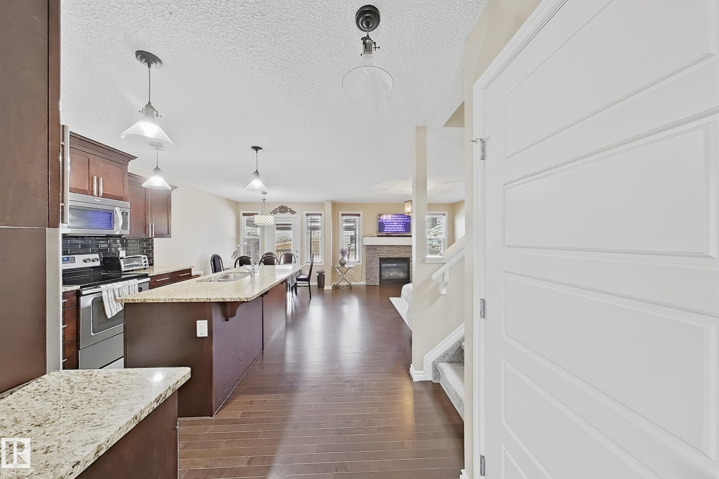 Open-concept living space featuring a kitchen with an extended island, wood-finish flooring, stainless steel appliances, a tile backsplash, and recessed lighting - 3609 Weidle Bend, Edmonton, AB - Indoor Photo Showing Kitchen