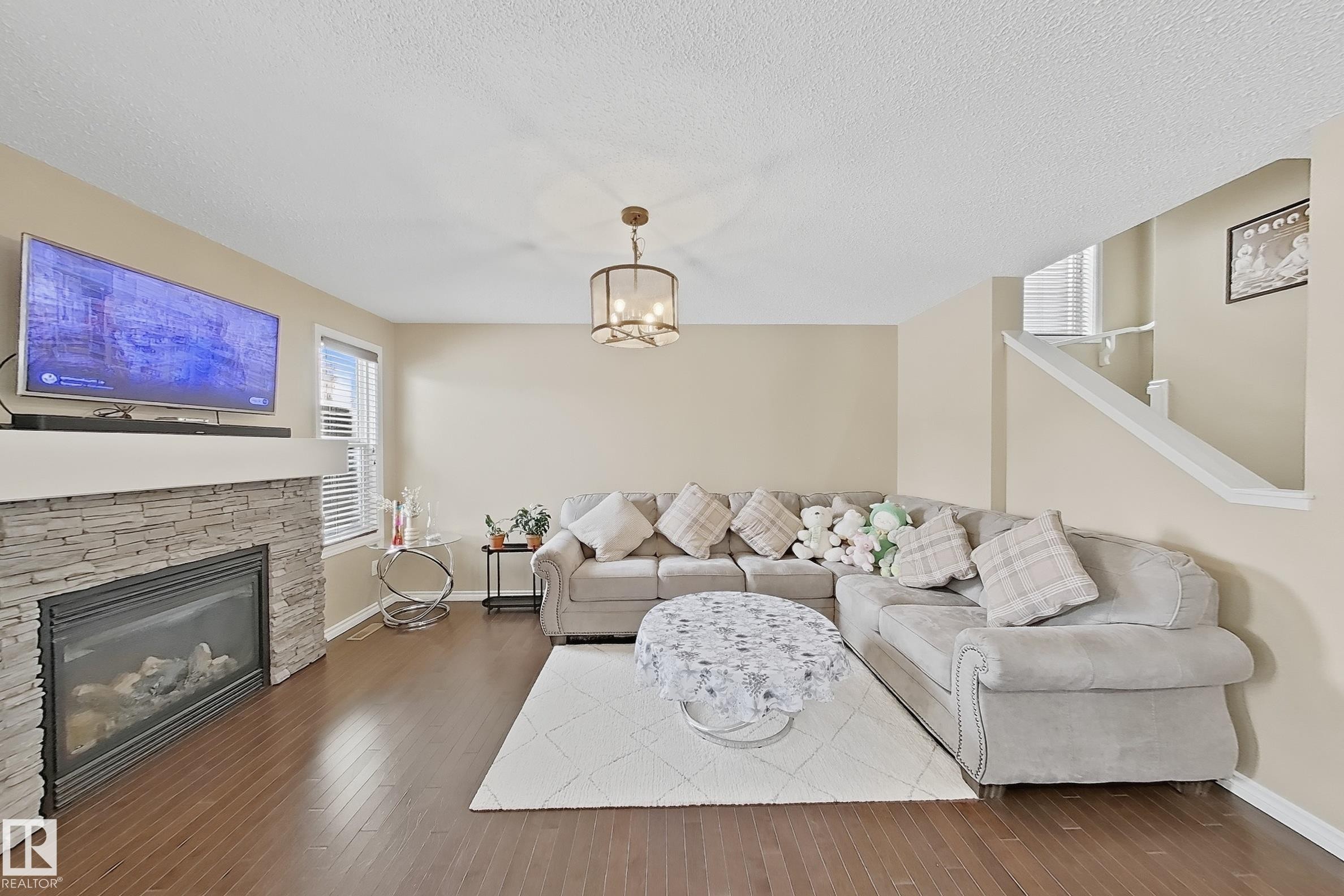 Living area featuring wood-finish flooring, a stacked stone fireplace with a white mantel, and windows on either side with blinds - 3609 Weidle Bend, Edmonton, AB - Indoor Photo Showing Living Room With Fireplace