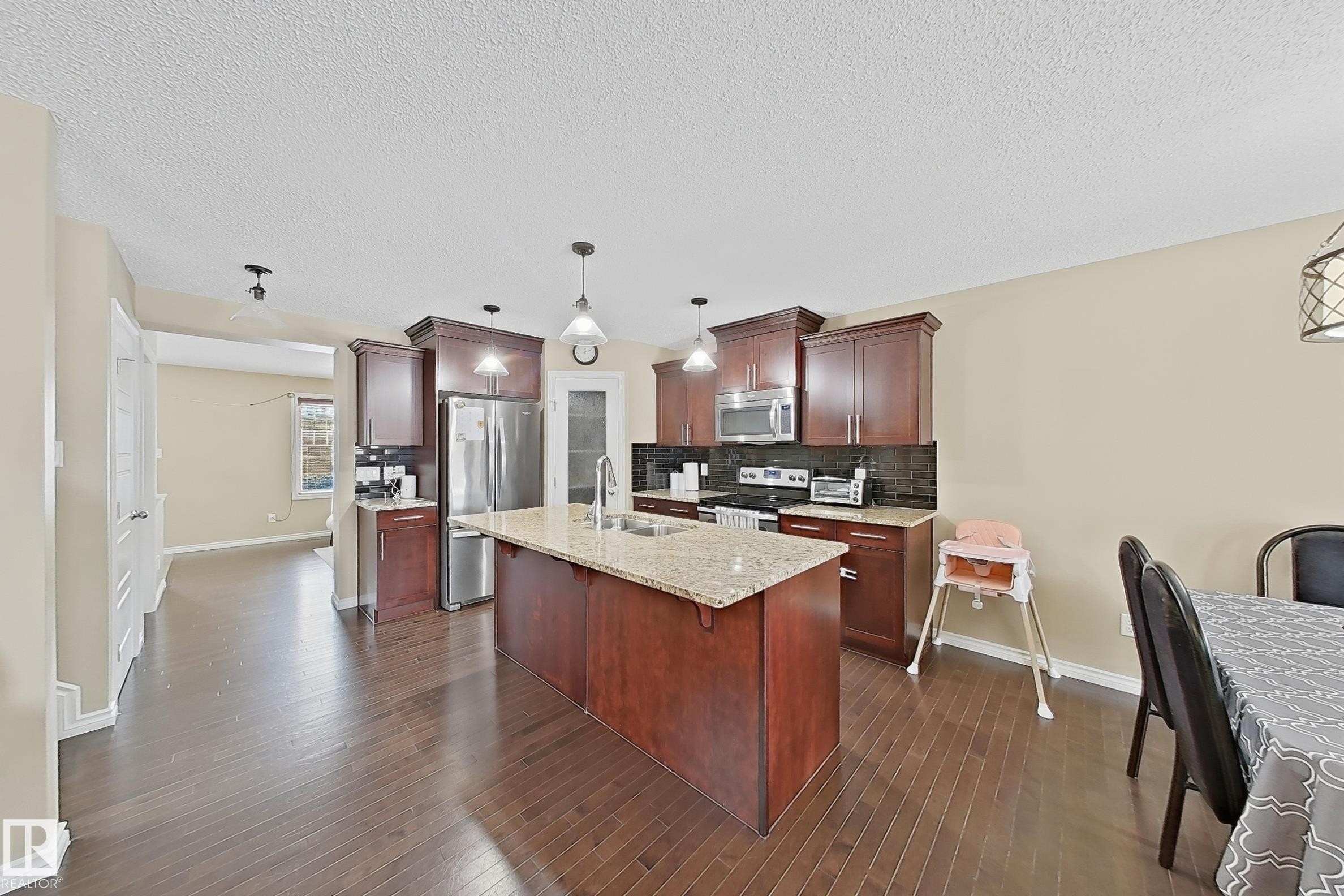 Kitchen featuring rich wood-finish cabinetry, granite-style countertops, and a dark tile backsplash - 3609 Weidle Bend, Edmonton, AB - Indoor Photo Showing Kitchen