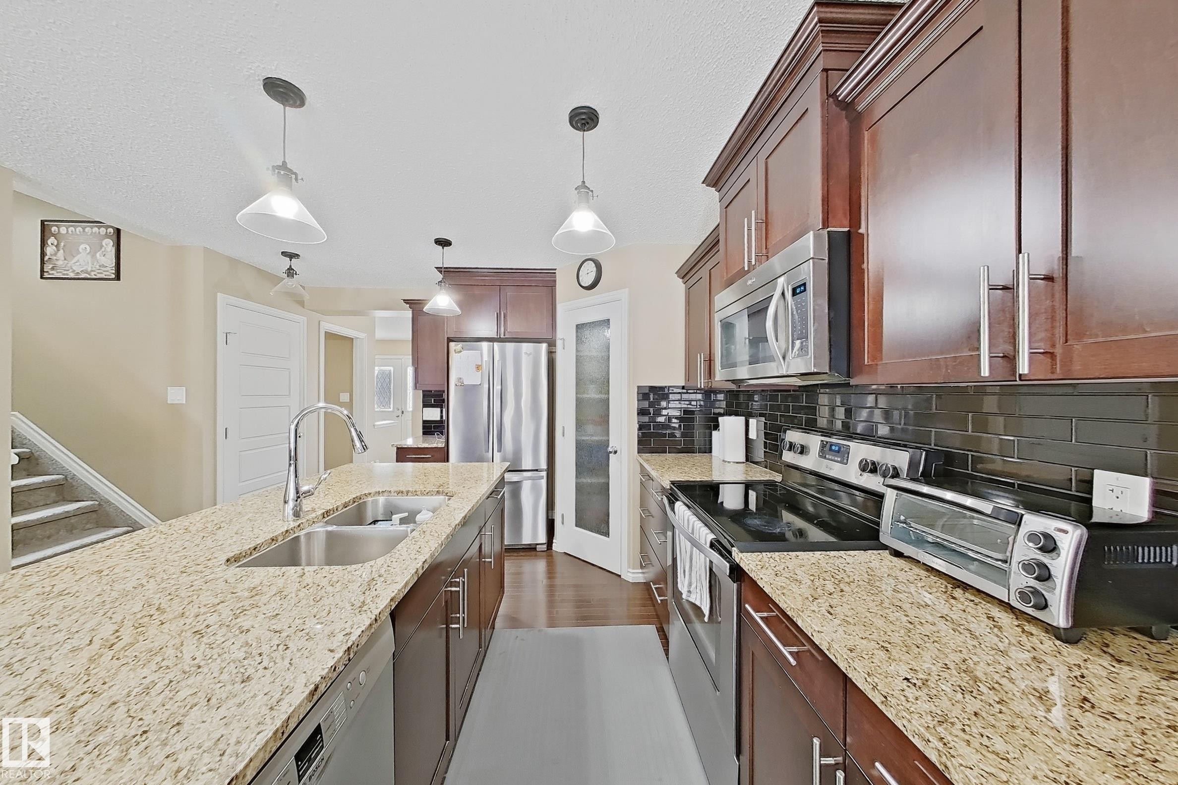 Spacious kitchen with granite countertops, rich wood cabinetry, stainless steel appliances, a double basin sink, and pendant lighting - 3609 Weidle Bend, Edmonton, AB - Indoor Photo Showing Kitchen With Double Sink With Upgraded Kitchen