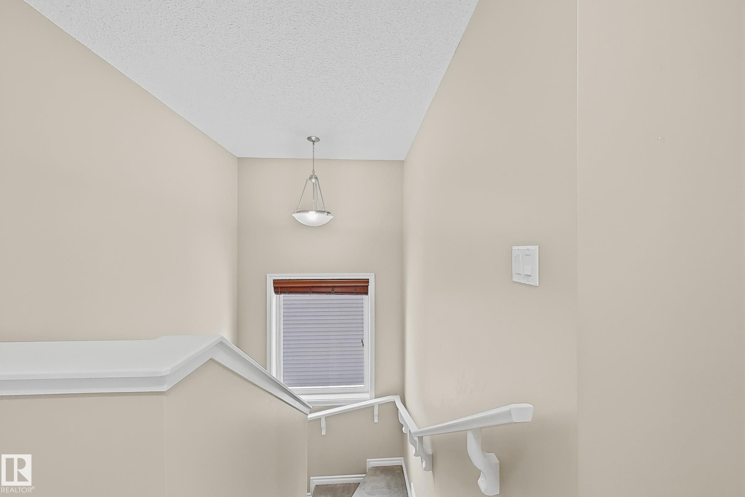 Stairwell with neutral wall paint and white trim, featuring a contemporary pendant light fixture, a window with horizontal blinds, and a white handrail with decorative brackets - 3609 Weidle Bend, Edmonton, AB - Indoor Photo Showing Other Room