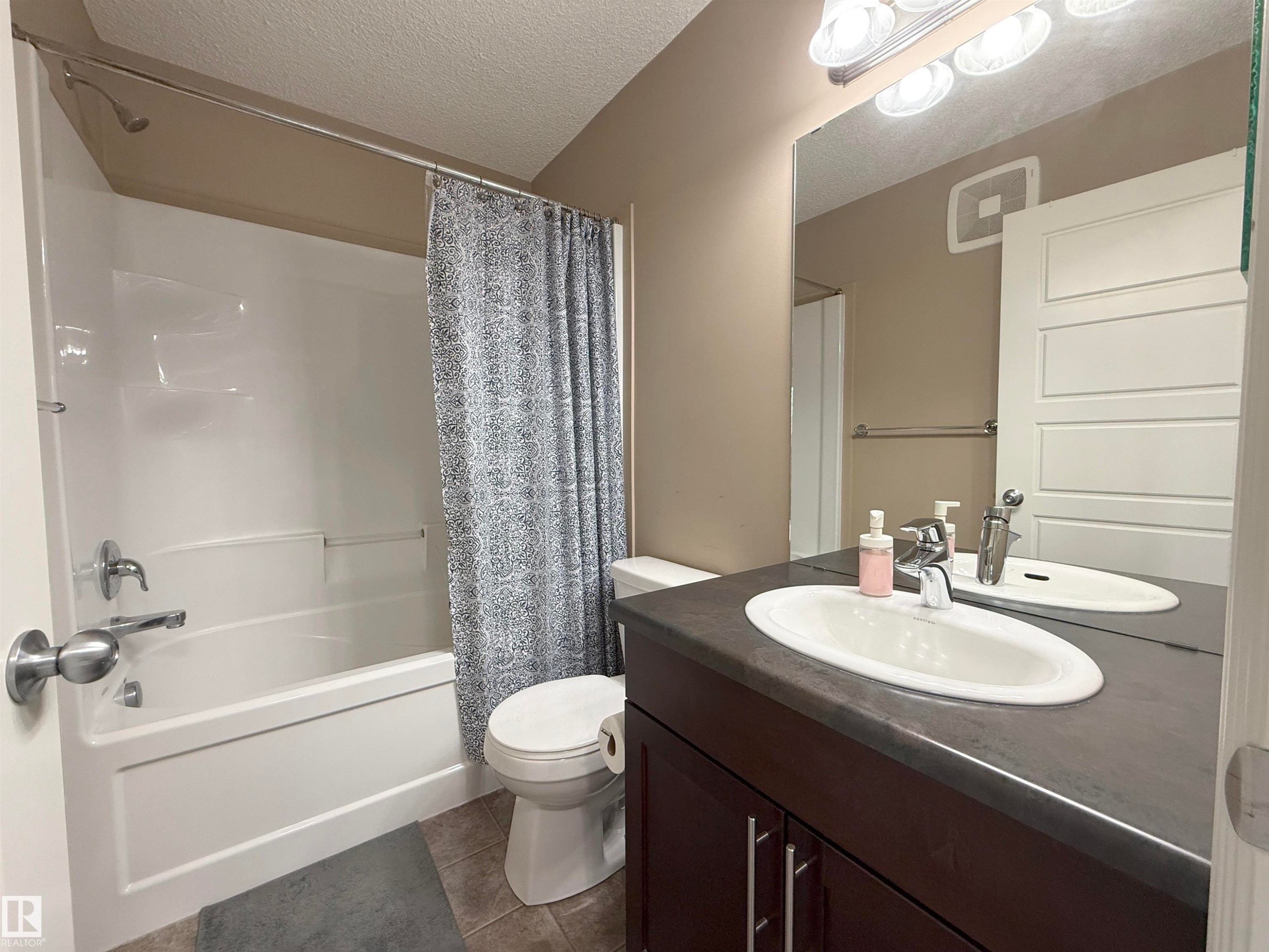 Bathroom featuring a white bathtub with chrome fixtures, a dark wood-finish vanity with a single sink and dark countertop, a full-width mirror, and a tile floor - 3609 Weidle Bend, Edmonton, AB - Indoor Photo Showing Bathroom
